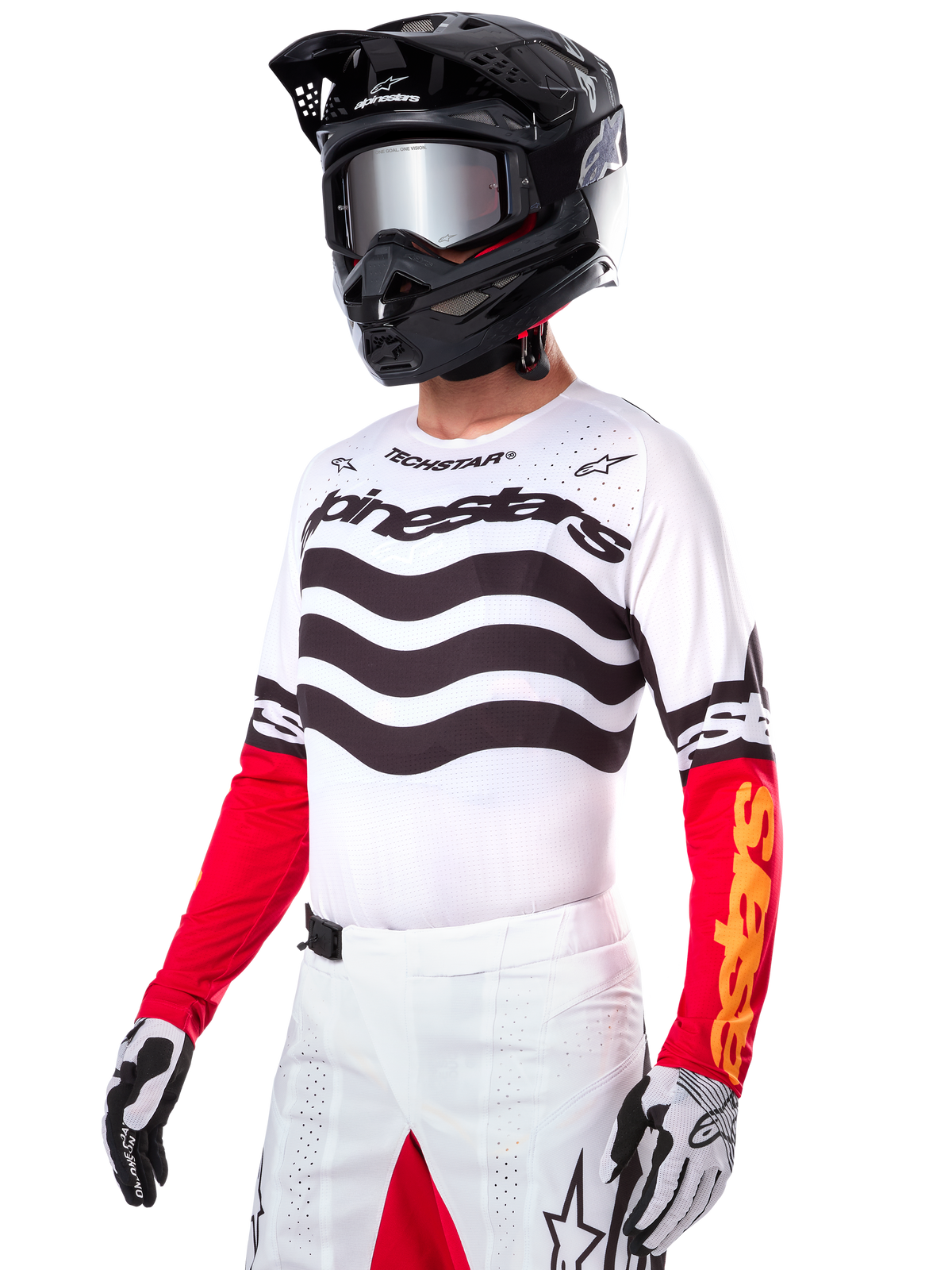 Alpinestars Limited Edition Techstar Deep Jersey, motorcrosser met een wit shirt met zwarte golvende strepen en rode onderkant van de mouwen, gecombineerd met een zwarte helm, spiegelende crossbril, wit-zwarte handschoenen en witte crossbroek, performance motorcross outfit.