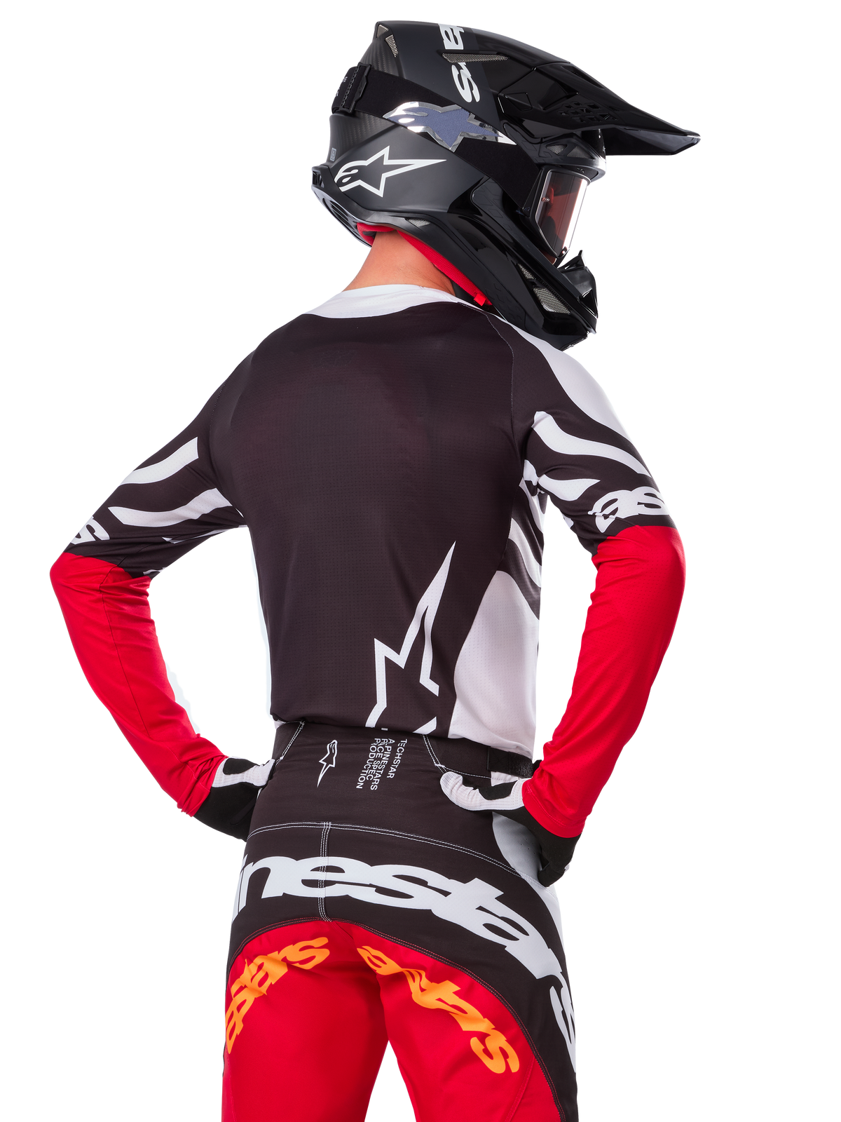 Motocross-Fahrer in kompletter Rennausrüstung, Alpinestars Limited Edition Techstar Deep Jersey in Schwarz, Weiß und High Red, Rückansicht, passende Techstar Deep Hose, schwarzer Helm mit Brille, schwarz-weiße Handschuhe, professionelles Offroad-Rennoutfit