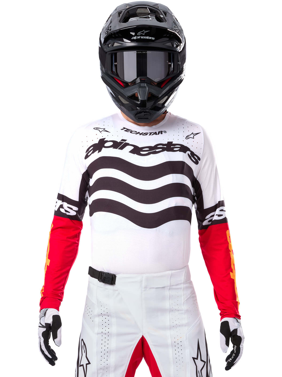 Motocross-Fahrer in kompletter Rennausrüstung, Limited Edition Techstar Deep Trikot in Weiß und Schwarz mit roten Ärmeln, wellenförmige Grafiken und markantes Alpinestars-Branding, weiße Motocross-Hose, schwarzer Helm und Brille, abgestimmtes Outfit für Offroad-Rennen