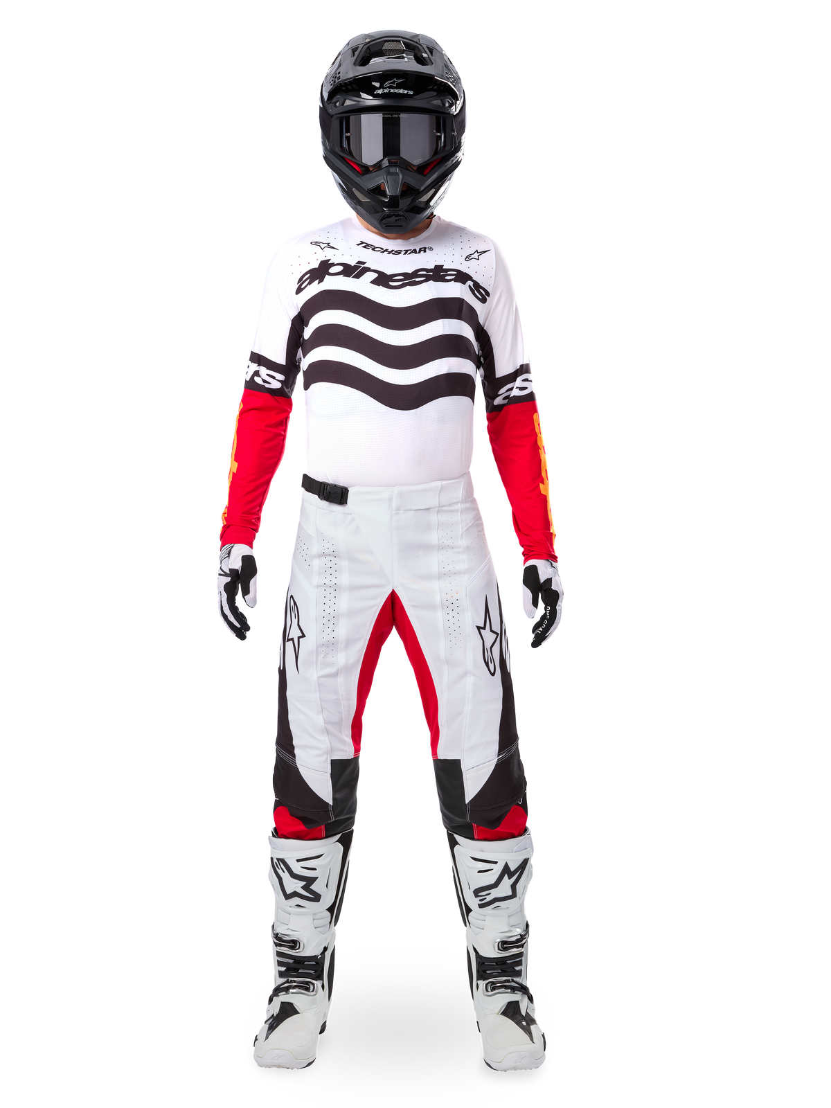 Pilote de motocross portant l'ensemble d'équipement Alpinestars Techstar Deep Édition Limitée, maillot blanc avec graphismes de vagues noirs et manches rouges, pantalon blanc et noir assorti avec accents rouges à l'intérieur des cuisses, casque noir avec lunettes sombres et bottes blanches, tenue de course tout-terrain professionnelle complète