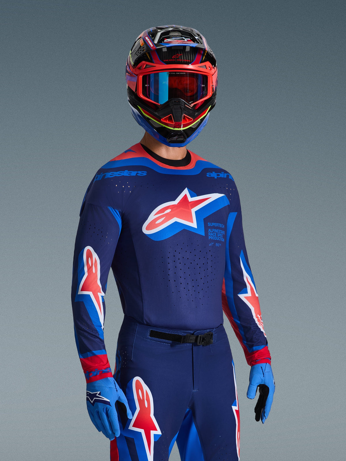 Alpinestars 2026 Supertech Vista Jersey in Dark Navy, Hot Coral en Cobalt, motorcrossrijder met bijbehorende broek en handschoenen, veelkleurige helm met rode bril, professionele kledingset voor off-road racing