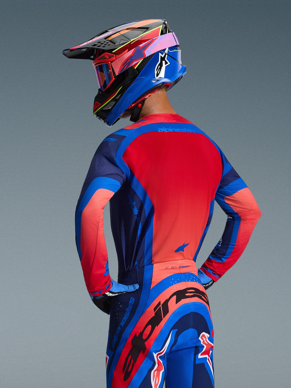 Achteraanzicht van een motocrossrijder die het Alpinestars 2026 Supertech Vista Jersey draagt in Dark Navy, Hot Coral en Cobalt, voorzien van een opvallend rood rugpaneel en naadloze constructie, gecombineerd met bijpassende broek en helm voor een complete racing-look.