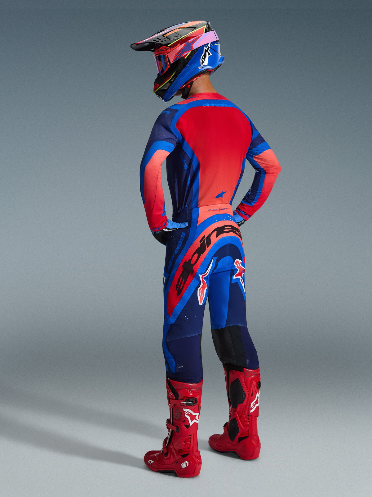 Motorcrosser van achteren gezien, Alpinestars 2026 Supertech Vista Jersey in Dark Navy, Hot Coral en Cobalt, gecombineerd met bijpassende motorcrossbroek, rode laarzen en een kleurrijke helm, gecoördineerde professionele race-uitrusting