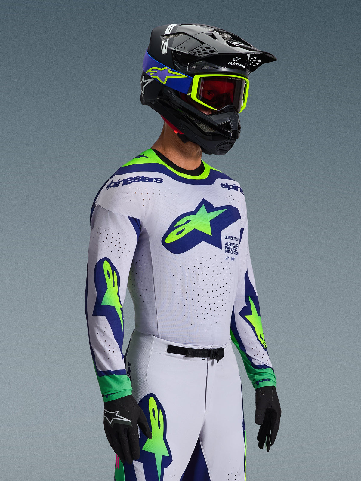 Ensemble d'équipement Alpinestars Supertech Vista 2026, maillot et pantalon de motocross, blanc avec accents bleus et vert citron, porté par un pilote avec un casque noir et des lunettes vert fluo, logos étoiles sur la poitrine et les manches, coupe de course athlétique de niveau professionnel pour la performance tout-terrain.