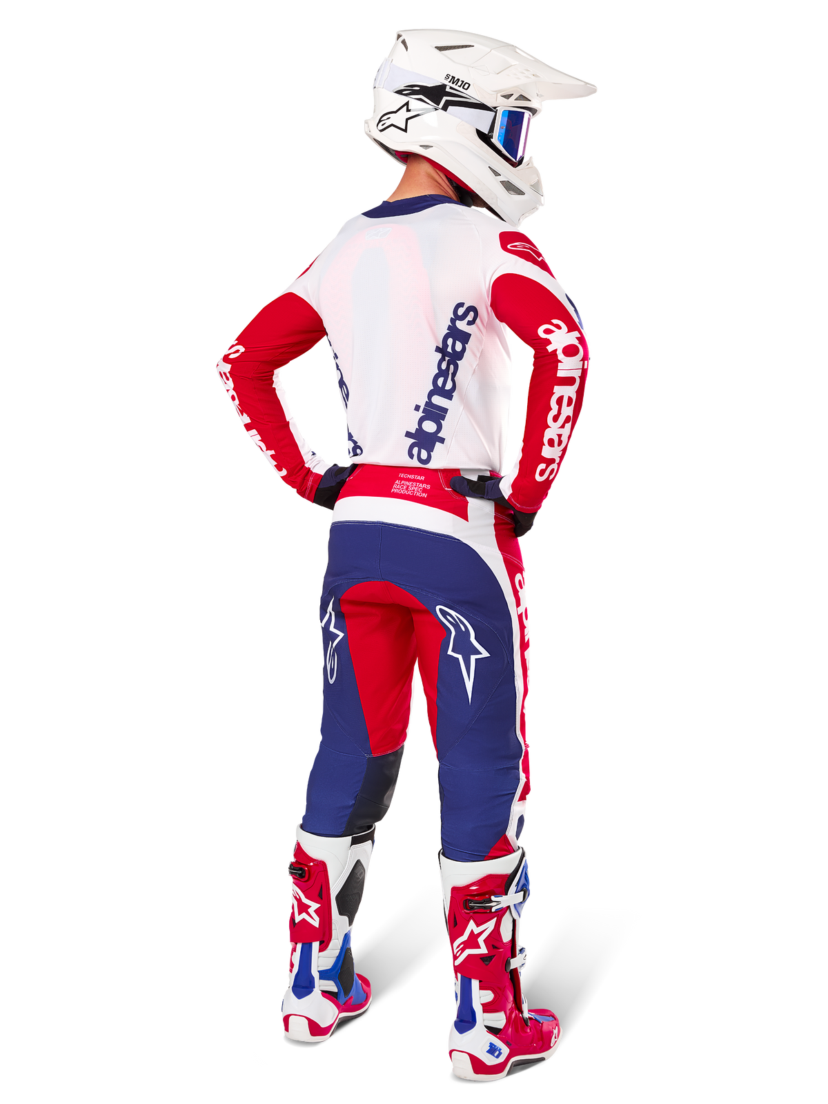 Motocross-Fahrer in der Rückansicht, trägt das Alpinestars Limited Edition Techstar Fortitude Trikot und Ausrüstungsset in der Farbkombination Bright Red White Blue, mit weißem Alpinestars-Branding auf den roten Ärmeln und einem marineblauen Logo auf dem weißen Rücken, kombiniert mit einem weißen Motocross-Helm und passenden Rennstiefeln.