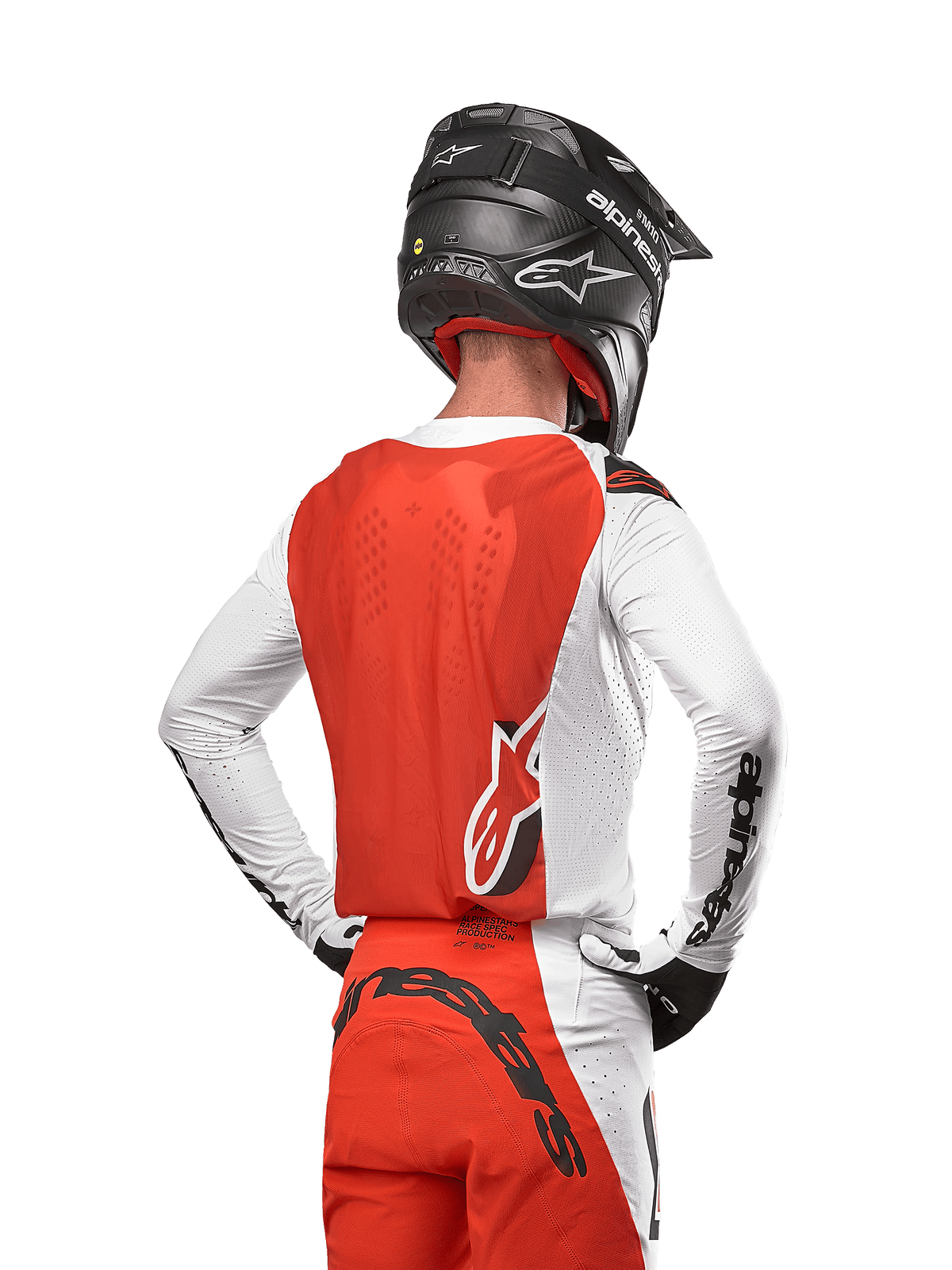 Pilote de motocross portant le maillot Supertech Ward 2024 en White Hot Orange, vue arrière montrant le panneau dorsal orange et les manches blanches avec logo Alpinestars noir, associé à un pantalon assorti et un casque noir, équipement professionnel coordonné pour la course tout-terrain