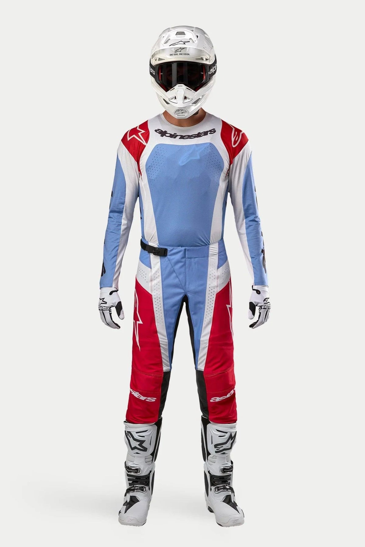 Pilote de motocross portant la tenue complète Alpinestars Techstar Ocuri 2024, maillot et pantalon bleu clair, rouge Mars et blanc, avec un casque blanc, des bottes blanches et des gants, équipement de course professionnel pour motocross tout-terrain