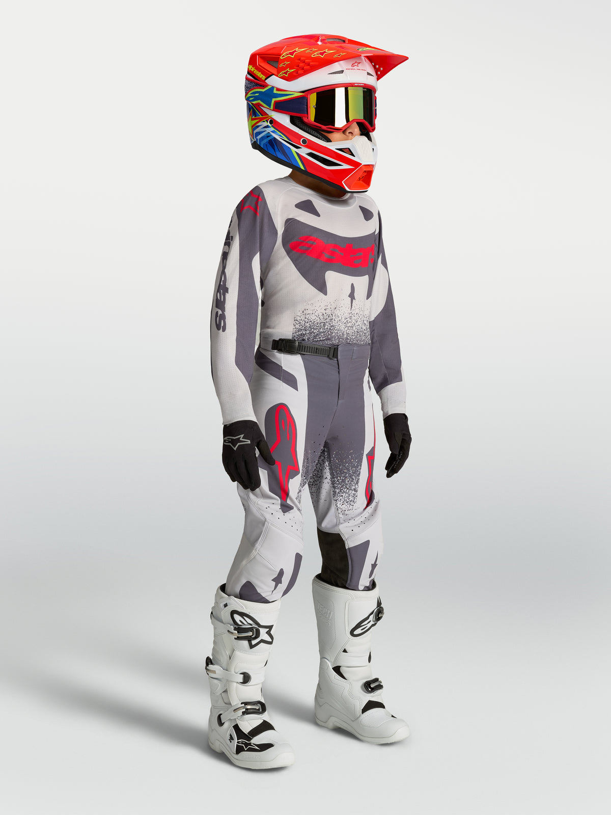 Alpinestars Supertech Swan Junior, maillot et ensemble de motocross, gris et rouge fluo, avec bottes de course blanches.