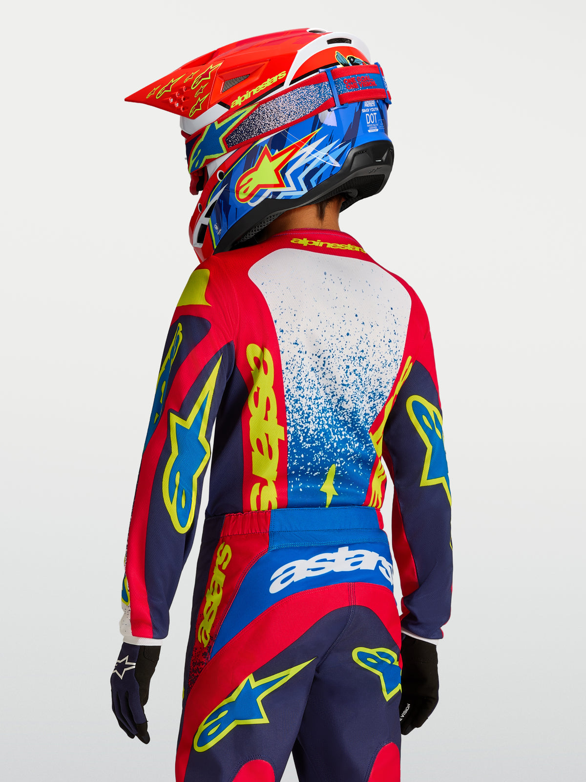 Maillot Fluid Drag Junior 2027 d'Alpinestars, maillot de motocross pour enfant, rouge et bleu marine avec graphismes jaunes, vue de dos sur un jeune pilote