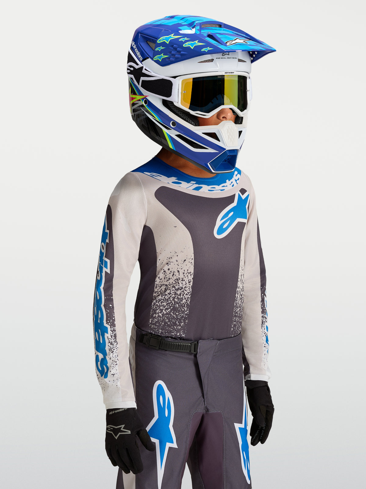 Alpinestars Fluid Jugend-Trikot Drag 2027, Motocross-Jugend-Trikot in Grau und Blau, getragen mit passendem Helm und Handschuhen, atmungsaktives Performance-Textil