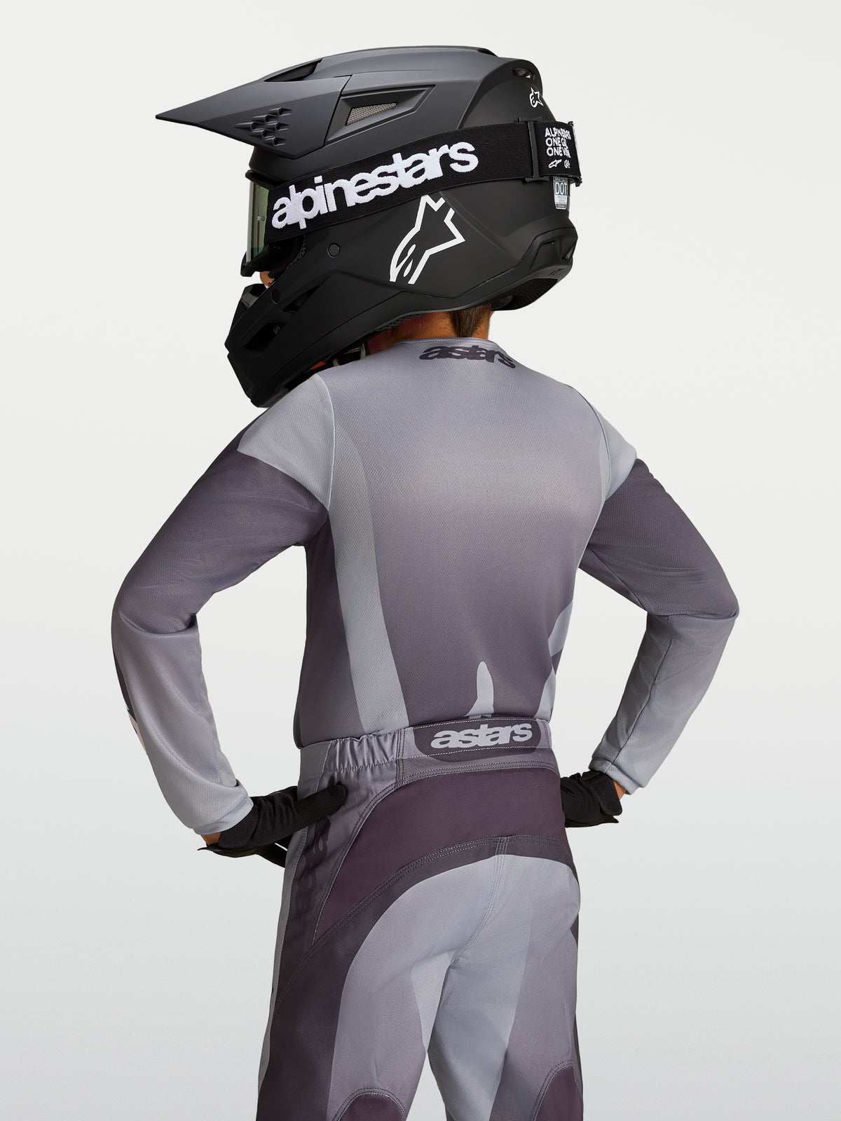 Alpinestars Maillot Fluid Amber Junior, maillot de motocross pour enfant, gris et sable, tissu respirant évacuant l'humidité, vue de dos sur un jeune pilote avec casque.