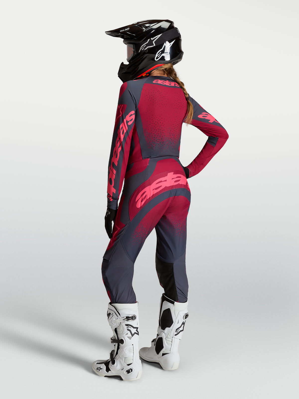 Alpinestars Stella Techstar Swan, ensemble maillot et pantalon de motocross pour femme, rouge et gris foncé, vue de dos montrant la coupe athlétique, avec casque noir et bottes blanches.
