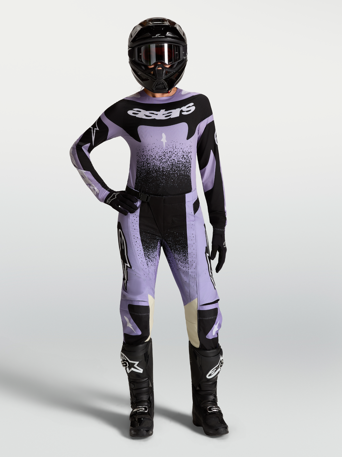 Pantalon Stella Techstar Swan Alpinestars, pantalon de motocross pour femme, violet et noir, conçu pour la performance tout-terrain, porté par une pilote avec tenue complète et casque.