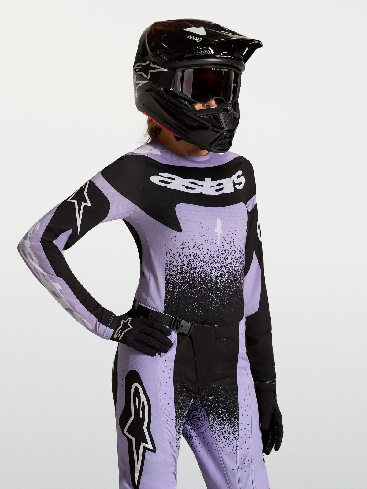 Maillot Alpinestars Stella Techstar Swan, haut de motocross pour femme, violet et noir, coupe athlétique de course, porté par une pilote avec équipement assorti.