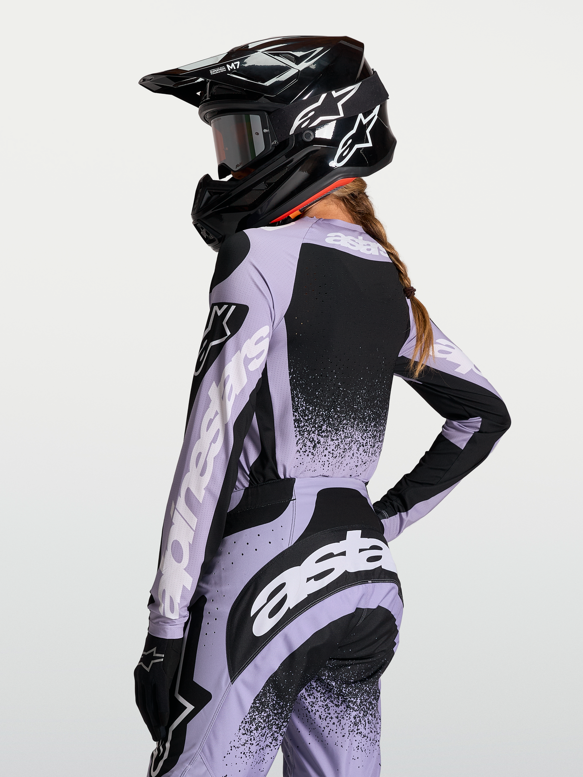 Maillot Stella Techstar Swan Alpinestars, haut de motocross pour femme, violet et noir, tissu respirant et coupe de course, vue de dos avec casque et logos blancs