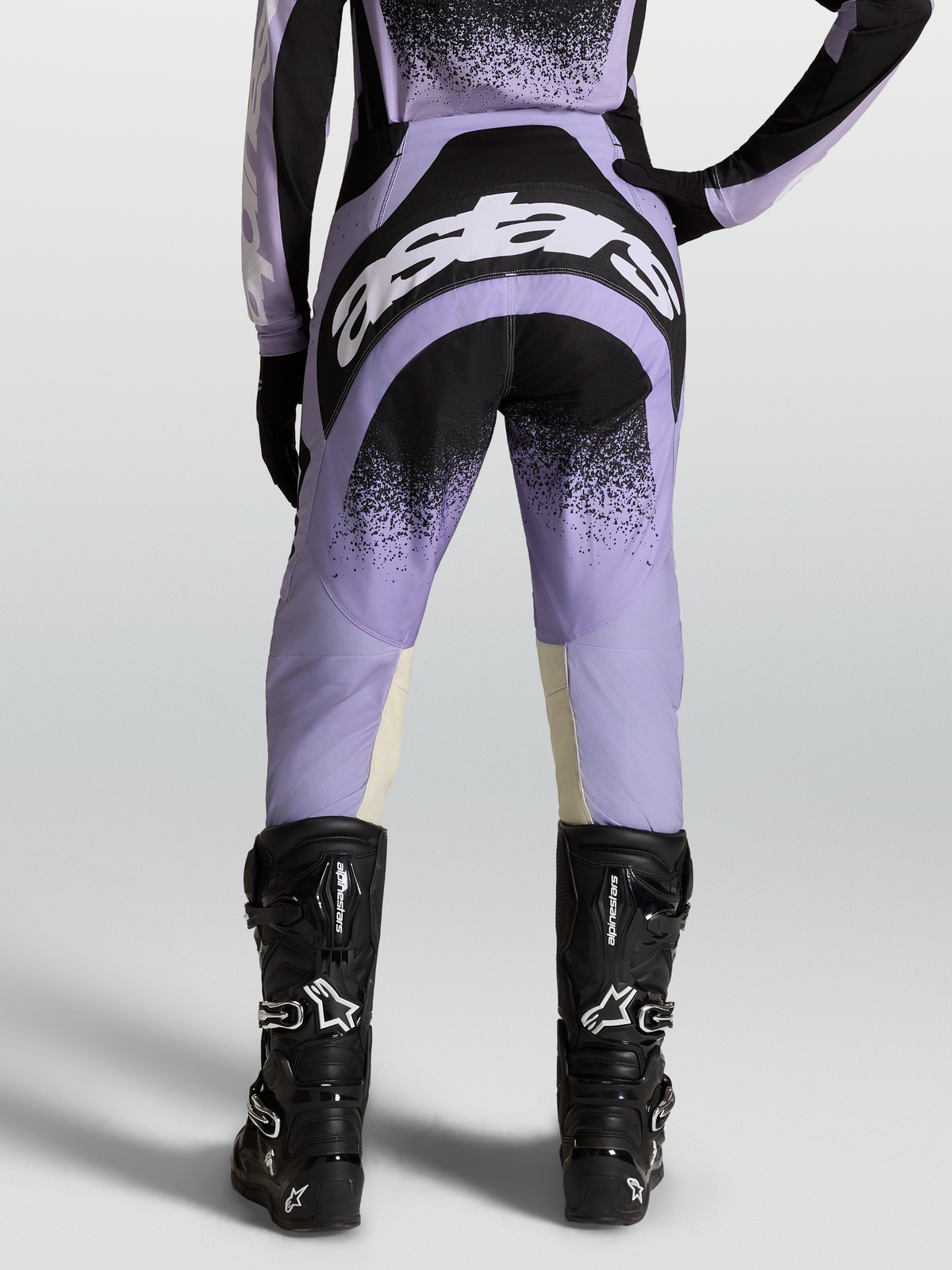 Alpinestars Stella Techstar Swan, pantalon de motocross pour femme, violet et noir, vue de dos avec logos blancs, porté par un mannequin avec des bottes de moto noires