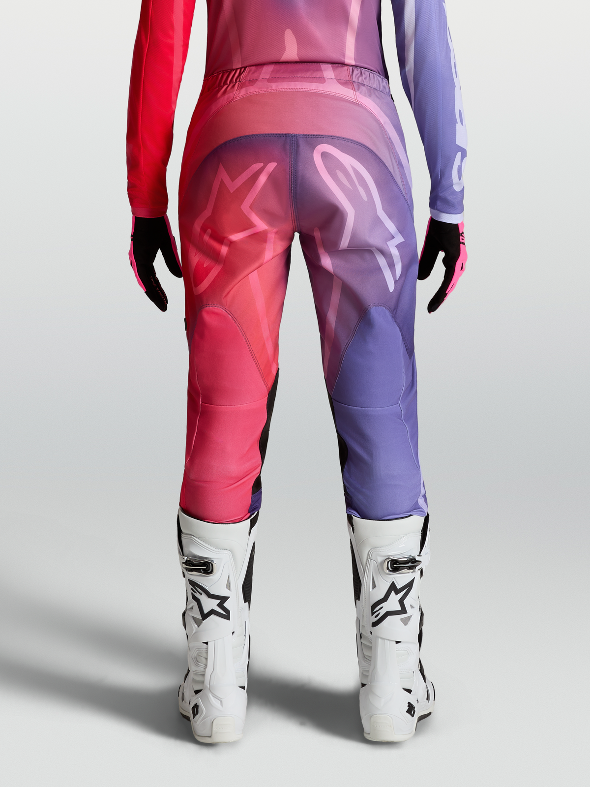 Alpinestars Stella Fluid Kepler, pantalon de motocross pour femme, rouge et violet, coupe ergonomique préformée avec logos Astars à l'arrière, porté avec des bottes de moto blanches.