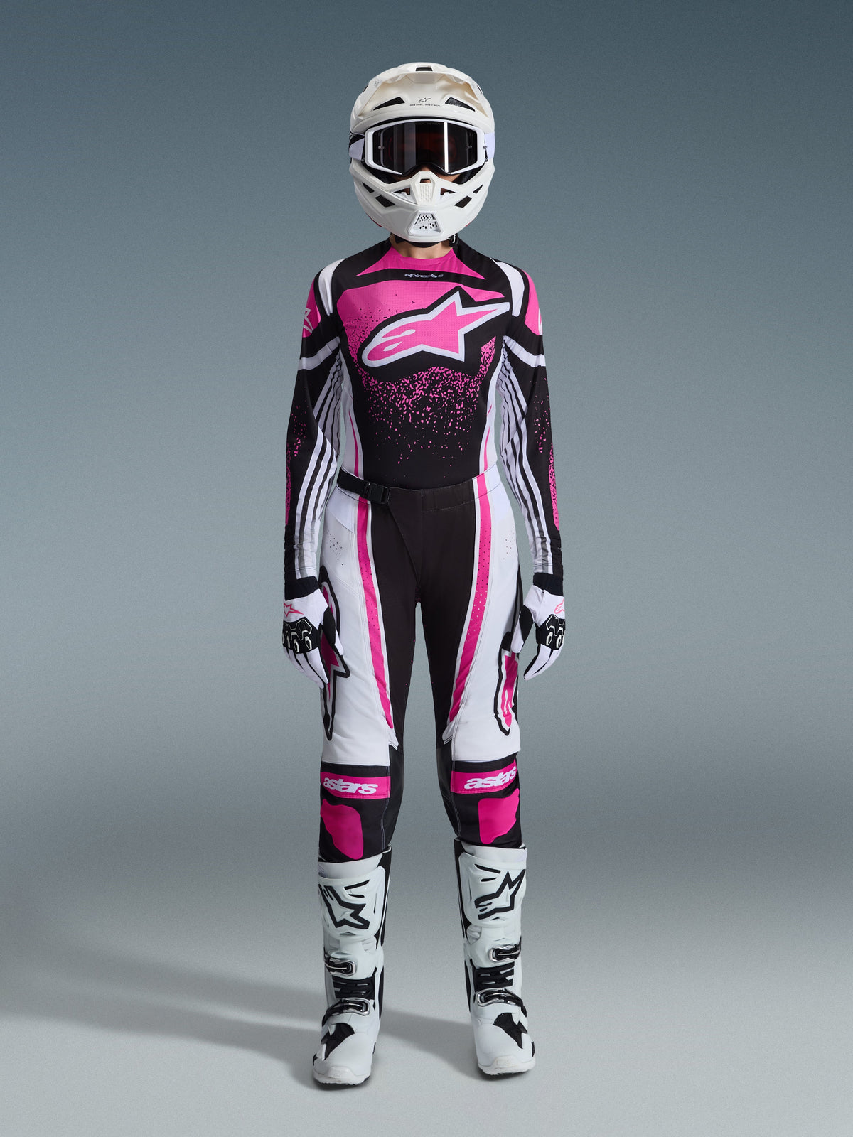 Alpinestars 2026 Stella Techstar Nomur, tenue de motocross complète pour femme en noir, blanc et fuchsia, maillot avec grand logo étoile et design d'éclaboussures roses, pantalon assorti, casque blanc avec lunettes, bottes noires et blanches, équipement tout-terrain coordonné