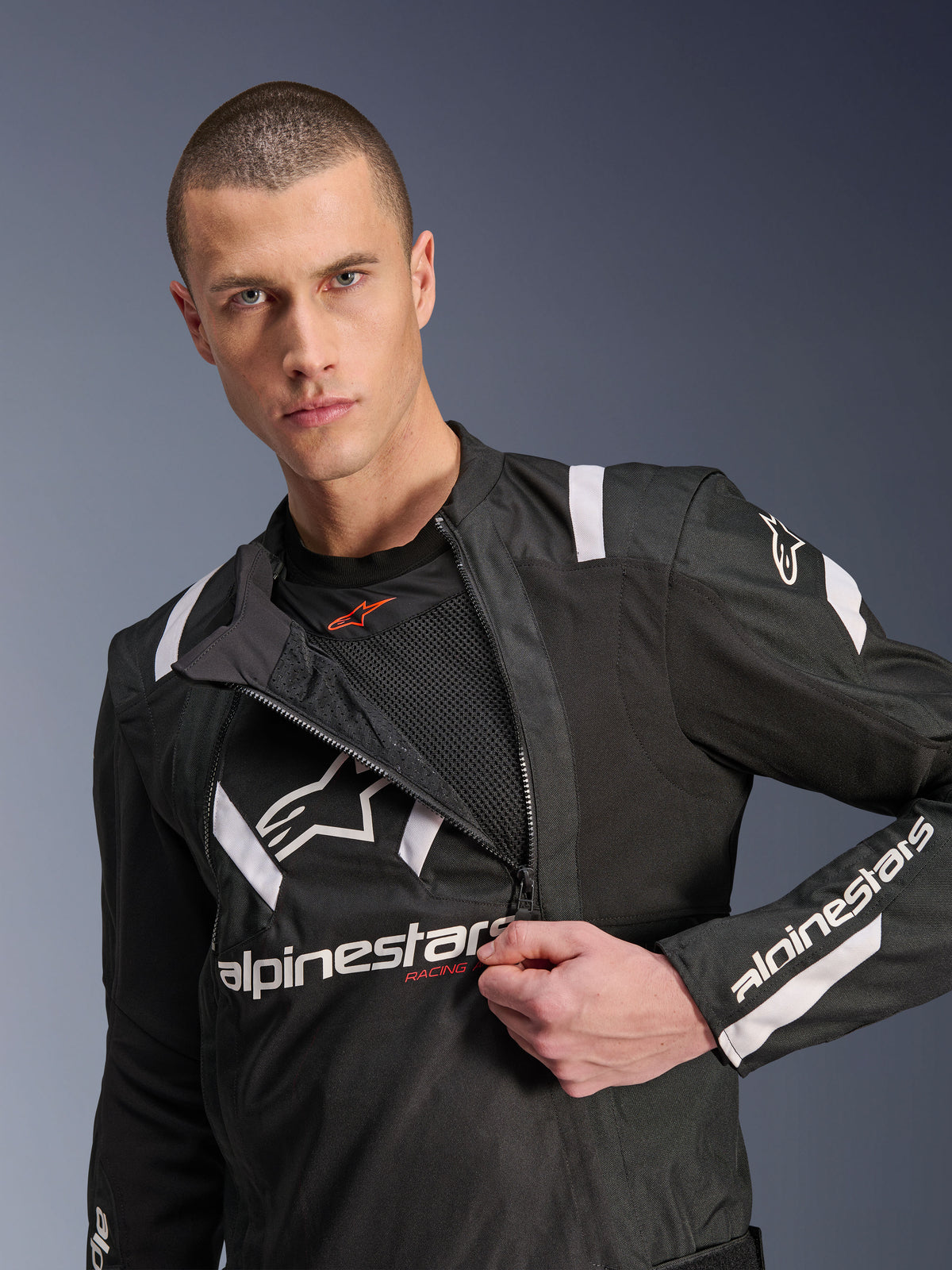 Alpinestars T-Stunt Air Jacket, Black and White motorcycle jacket, male model showing partially unzipped modular front panel revealing mesh airflow layers, white Alpinestars logos on chest and sleeves, sporty design for road riding