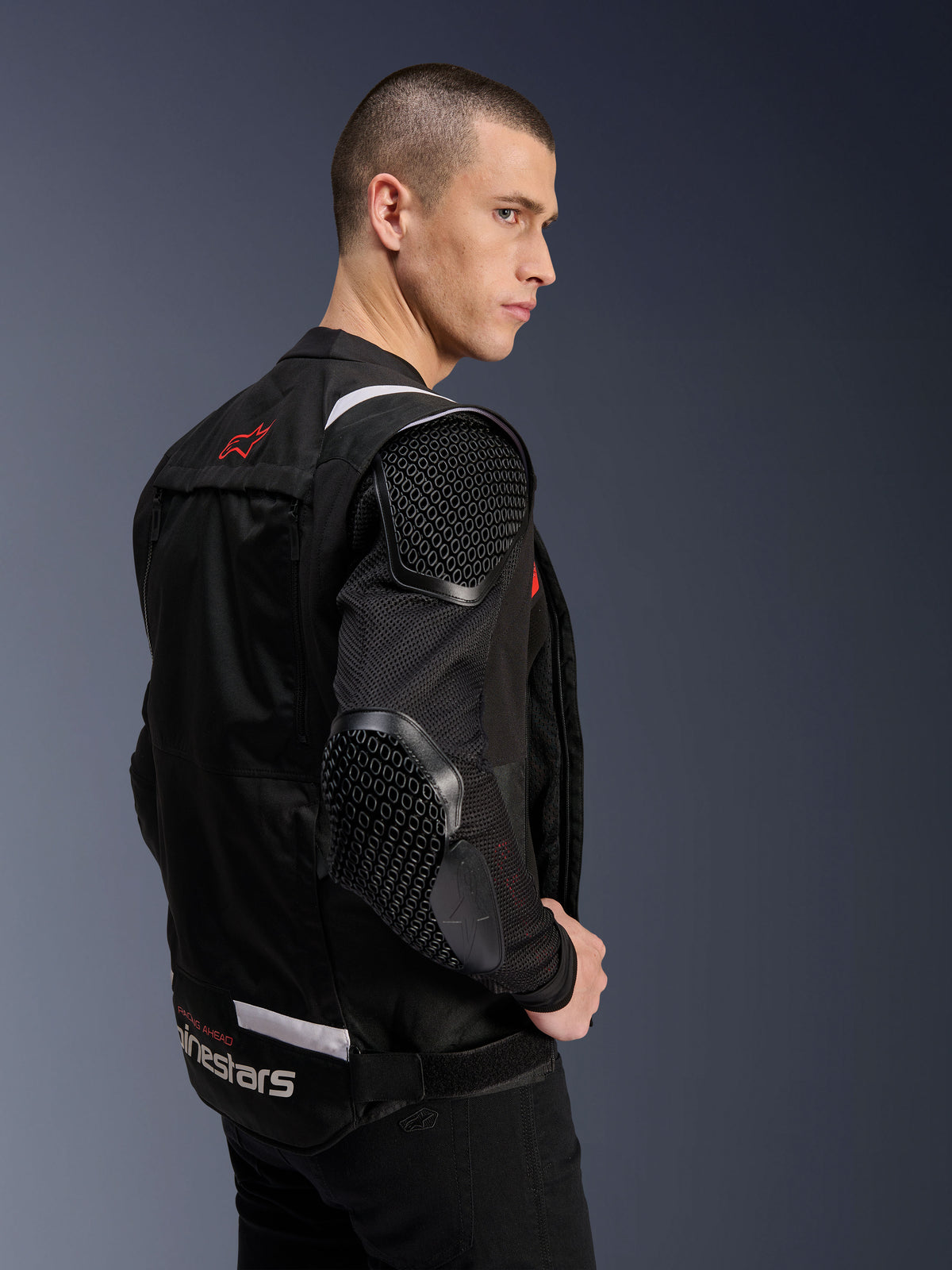 Alpinestars T-Stunt Air Jacket, Motorcycle Jacket, Black, side profile of a model wearing the sport-cut jacket with mesh sleeves and visible honeycomb-patterned armor on the shoulder and elbow, red logo on the back, white branding at the waist.