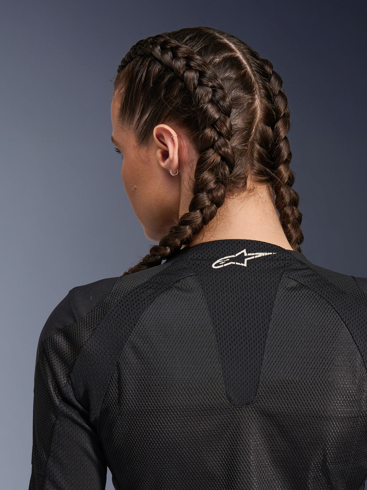 Veste Alpinestars Stella Troop-Air pour femme, noire, vue arrière détaillée du haut du dos et de la nuque, femme avec des tresses françaises, logo Astars blanc sur le col et tissu technique en maille 2D légère pour la ventilation