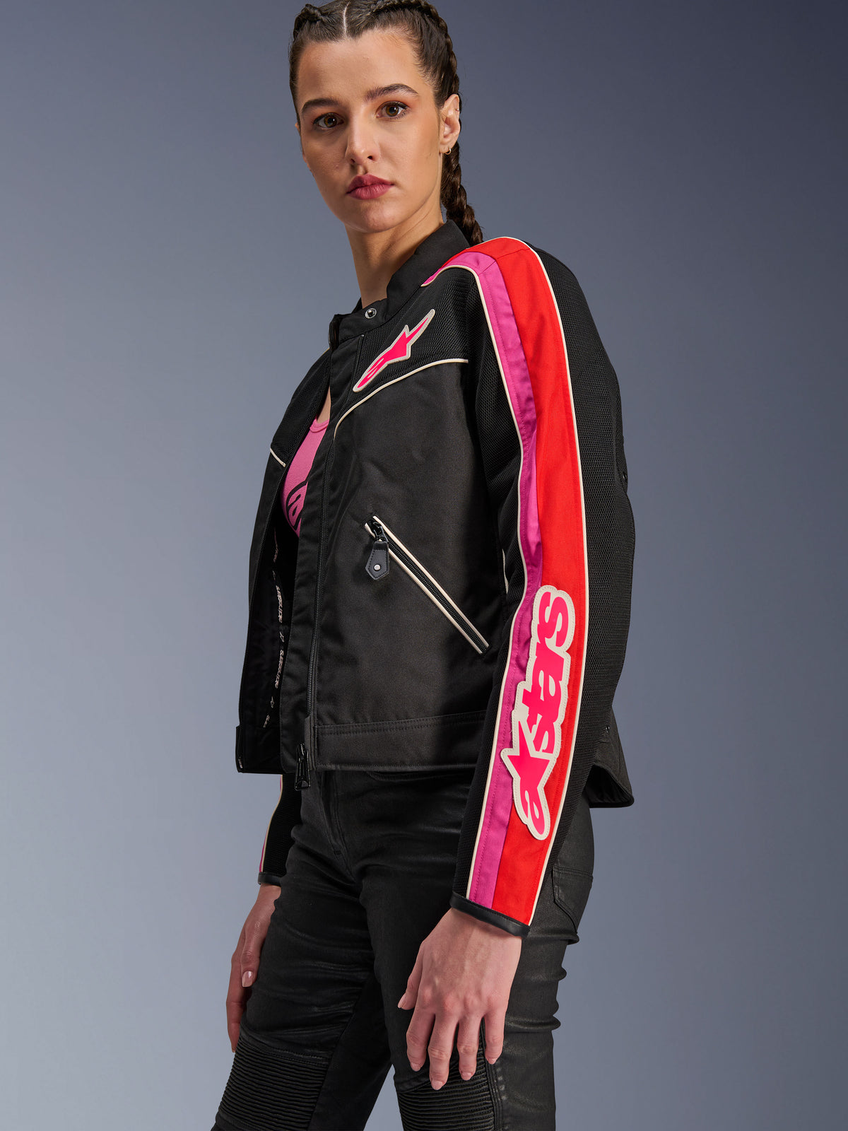 Alpinestars Stella T-Dyno Air Damenjacke, Damen-Motorradjacke, Schwarz mit leuchtend roten und fuchsiafarbenen Akzenten, getragen mit einer schwarzen Hose, mit pinkem Astars-Logo auf der Brust und am Ärmel, taillierte Biker-Passform mit Mesh-Einsätzen zur Belüftung.