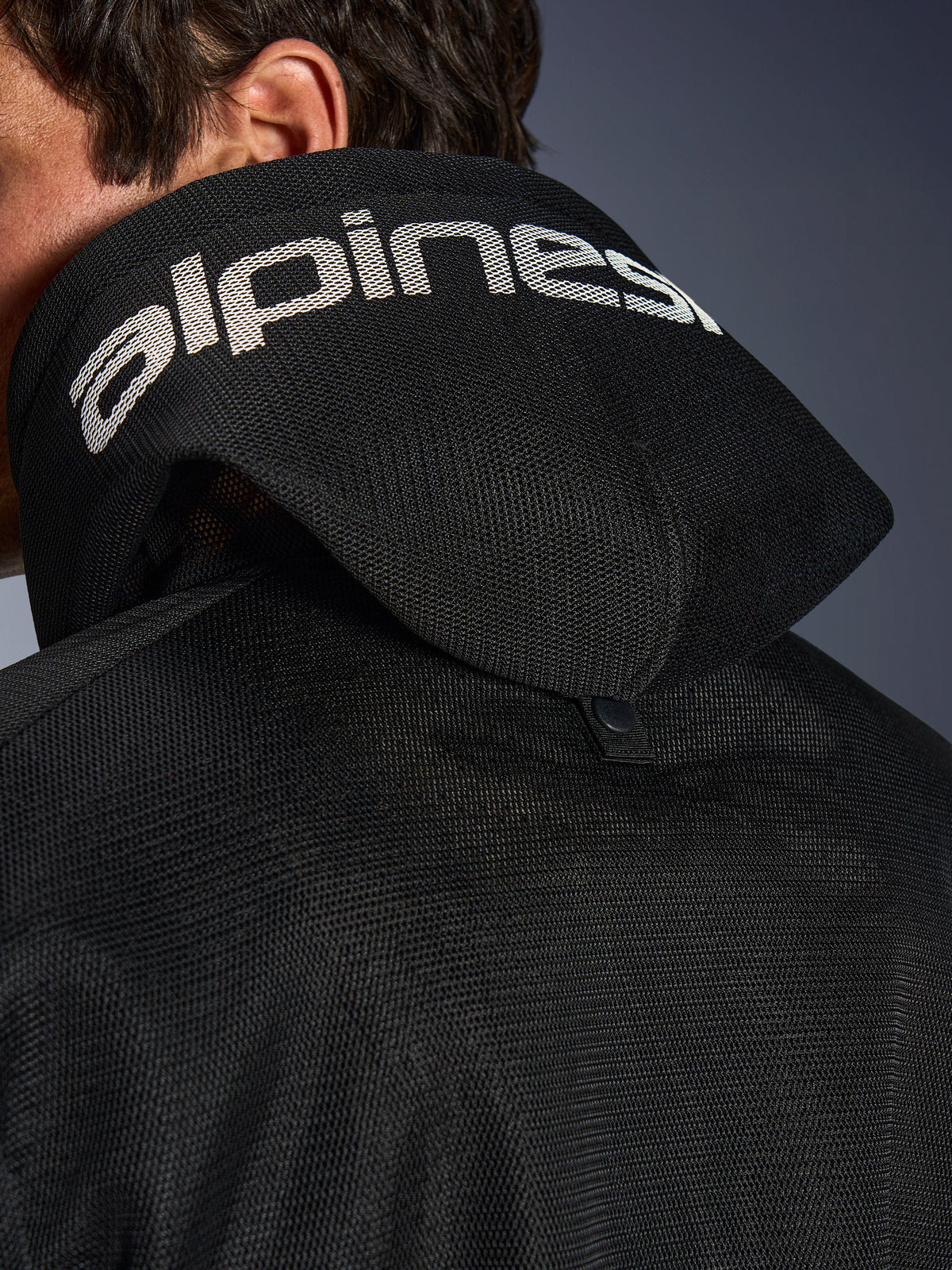 Alpinestars Chrome Superairflow Hoodie, Schwarz, Detailansicht der 3D-Mesh-Kapuze mit weißem Alpinestars-Branding auf der Oberseite, zeigt den rückseitigen Stabilisierungs-Druckknopf, belüftete Textil-Motorradausrüstung für extreme Hitze