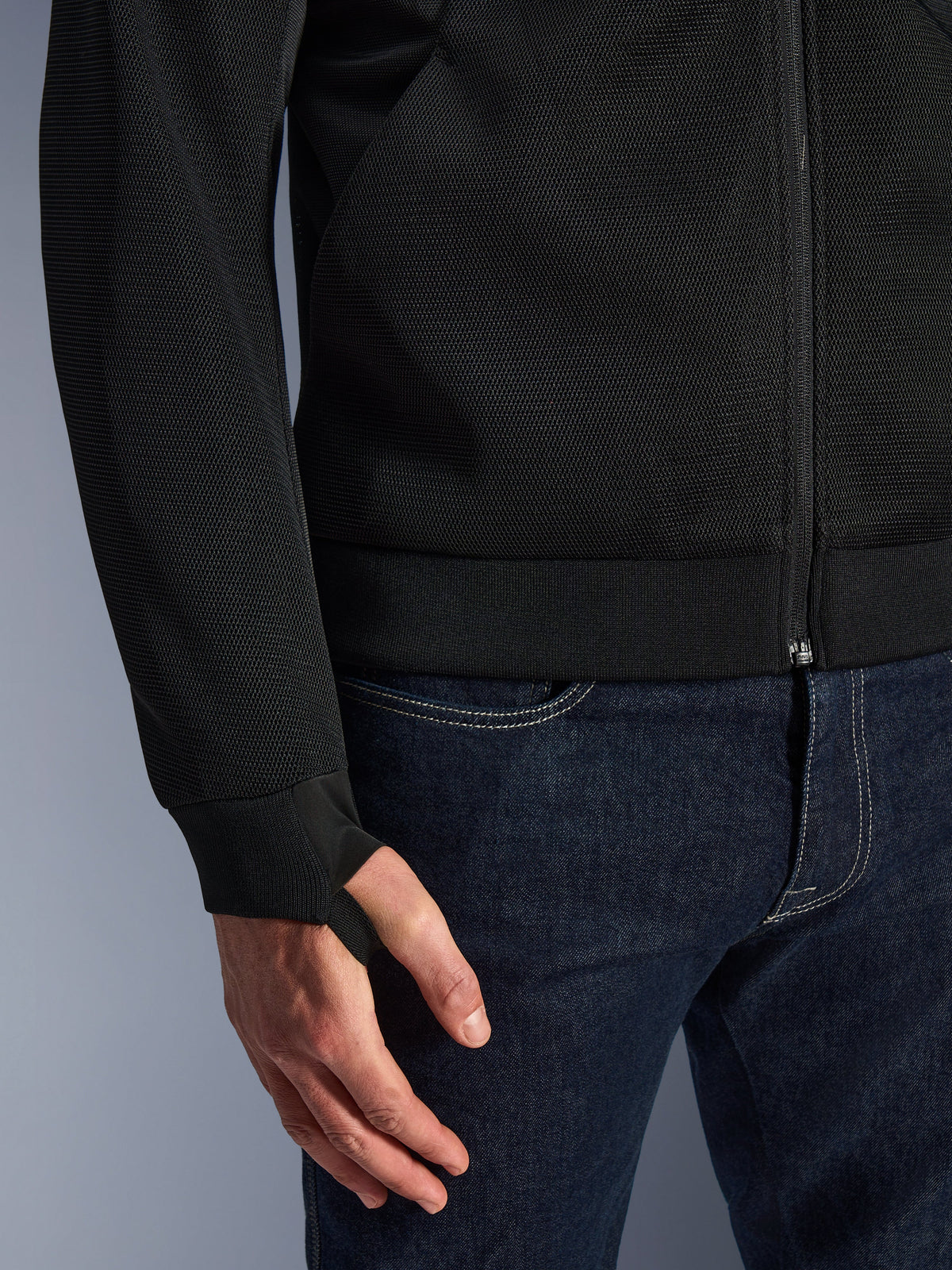 Alpinestars Chrome Superairflow Hoodie, Schwarz, Nahaufnahme des hochbeständigen technischen 3D-Mesh-Gewebes, mit geripptem Stretch-Jersey-Bündchen und elastischer Daumenschlaufe, getragen mit blauen Jeans