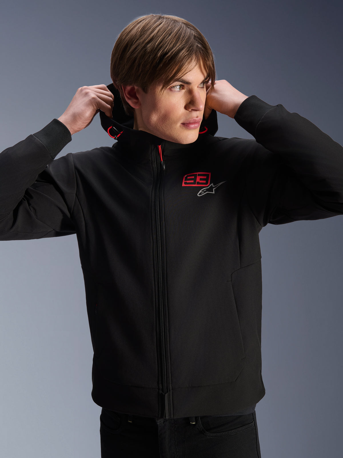 Alpinestars MM93 Radium Tech Hoodie, urban motorjas, zwart met rode en zilveren logo's, gedragen door een mannelijk model, voorzien van een volledige ritssluiting en geribbelde manchetten, casual lifestyle motorsportkleding