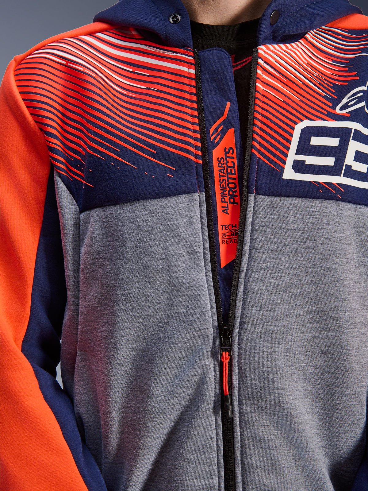 Alpinestars MM93 Chrome V2 Sport Hoodie, close-up van borst en kraag, navyblauw en grijs melange tech fleece met fluo rode graphics, voorzien van het witte 93-logo en Alpinestars Protects-branding op de binnenste ritsflap, Tech-Air Ready motorkleding