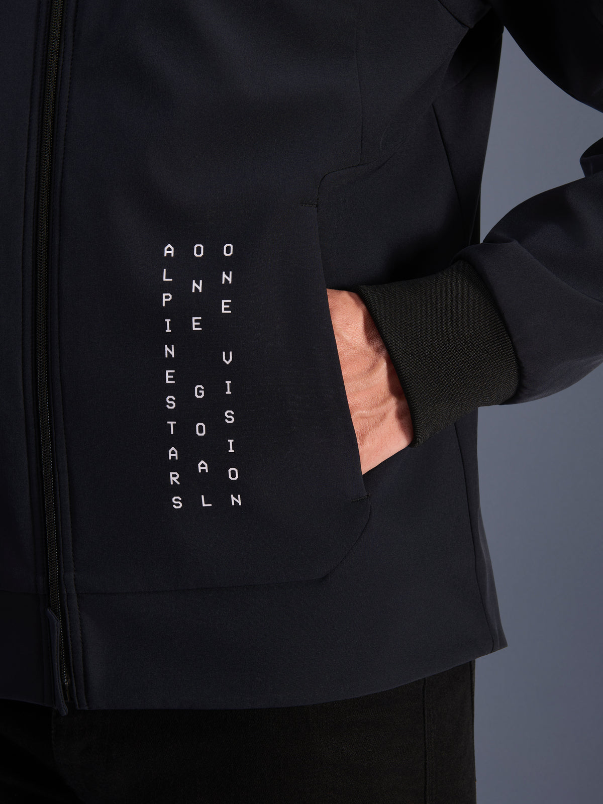 Alpinestars Radium Tech Kapuzenjacke, Herren Urban Motorradjacke, Schwarz mit weißem vertikalem Text und winddichtem Bündchen.