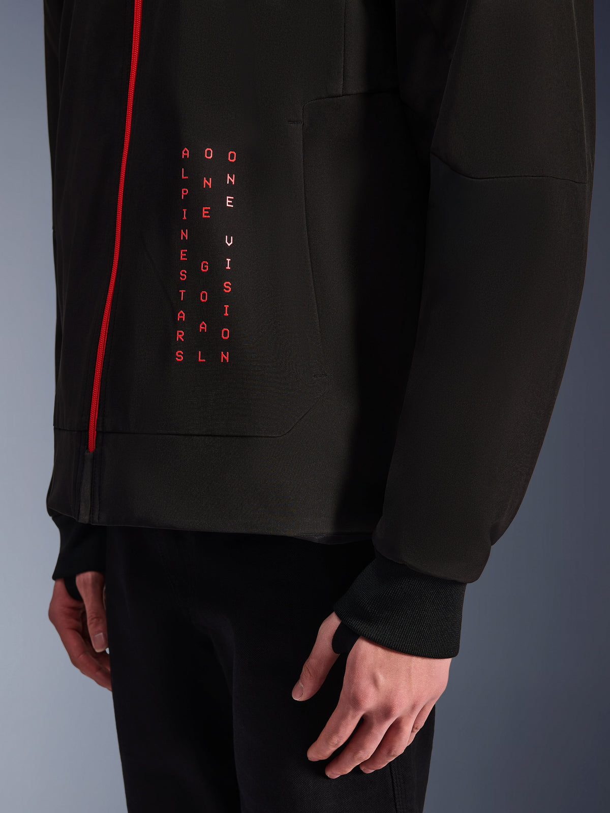 Alpinestars Radium Tech Hoodie, stedelijke motorjas, zwart en felrood, close-up van graphic aan de voorzijde met verticale rode tekst "ALPINESTARS ONE GOAL ONE VISION", rode rits en geribde manchet met duimgat.