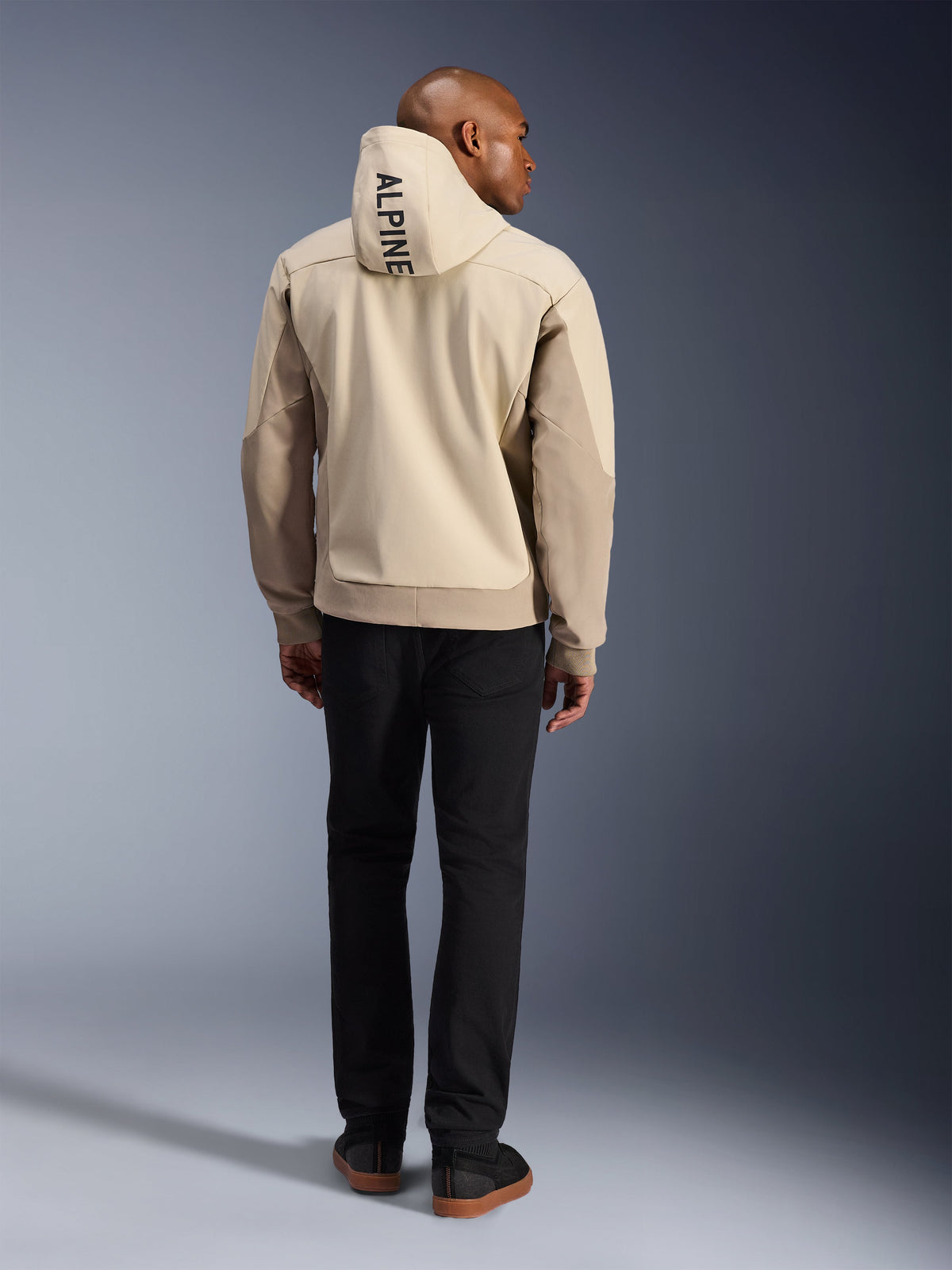 Alpinestars Radium Tech Hoodie, Mastic Aluminum, Rückansicht mit vertikalem „ALPINE“-Schriftzug auf der Kapuze, technische winddichte 3L-Shell Urban-Motorradjacke mit beigen Einsätzen, getragen mit schwarzer Hose