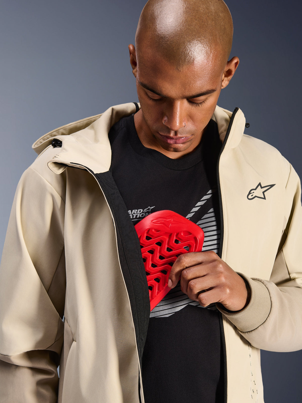 Alpinestars Radium Tech Hoodie in Mastic Aluminum, Urbane Motorradjacke, Modell zeigt interne Protektorentasche mit rotem Nucleon Brustprotektor, winddichtes Tech-Shell mit lässigem Hoodie-Design und Alpinestars-Branding.
