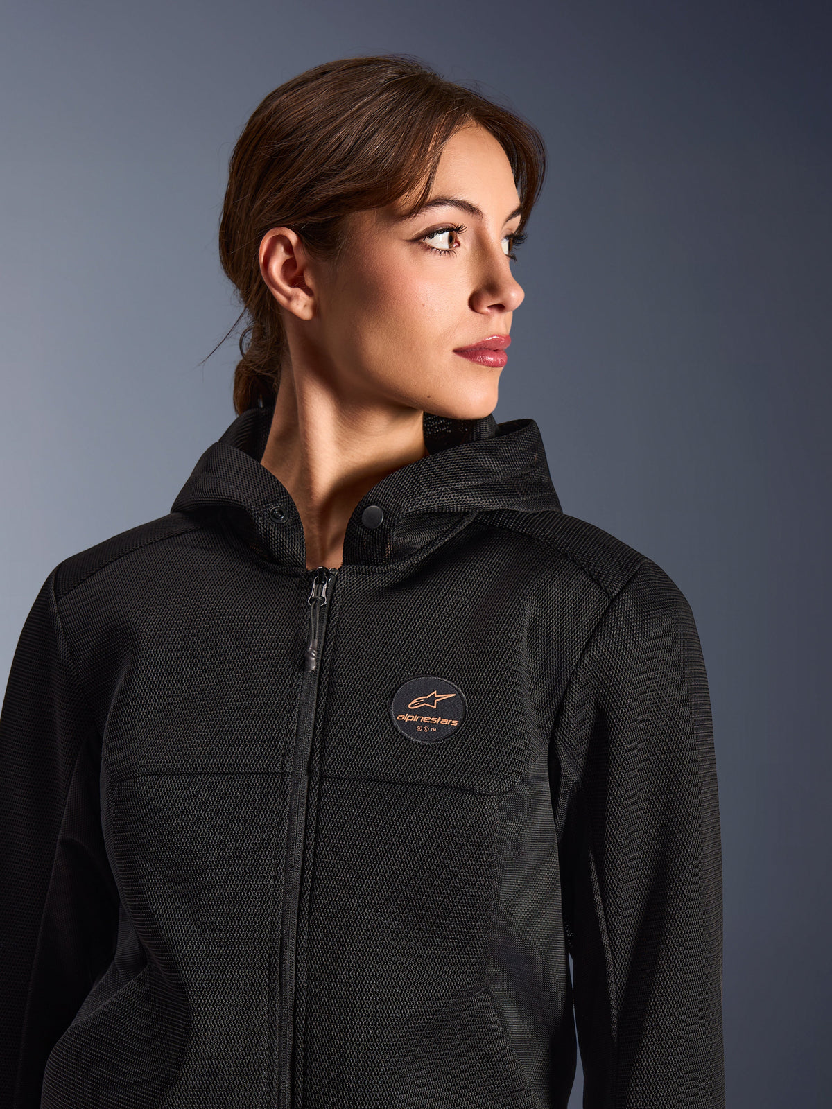 Frau trägt den Alpinestars Stella Chrome Superairflow Hoodie, Schwarz mit kupferfarbenem Logo, 3D-Mesh-Konstruktion für maximale Belüftung, technische Motorradbekleidung für Damen, urbaner sportlicher Fahrstil