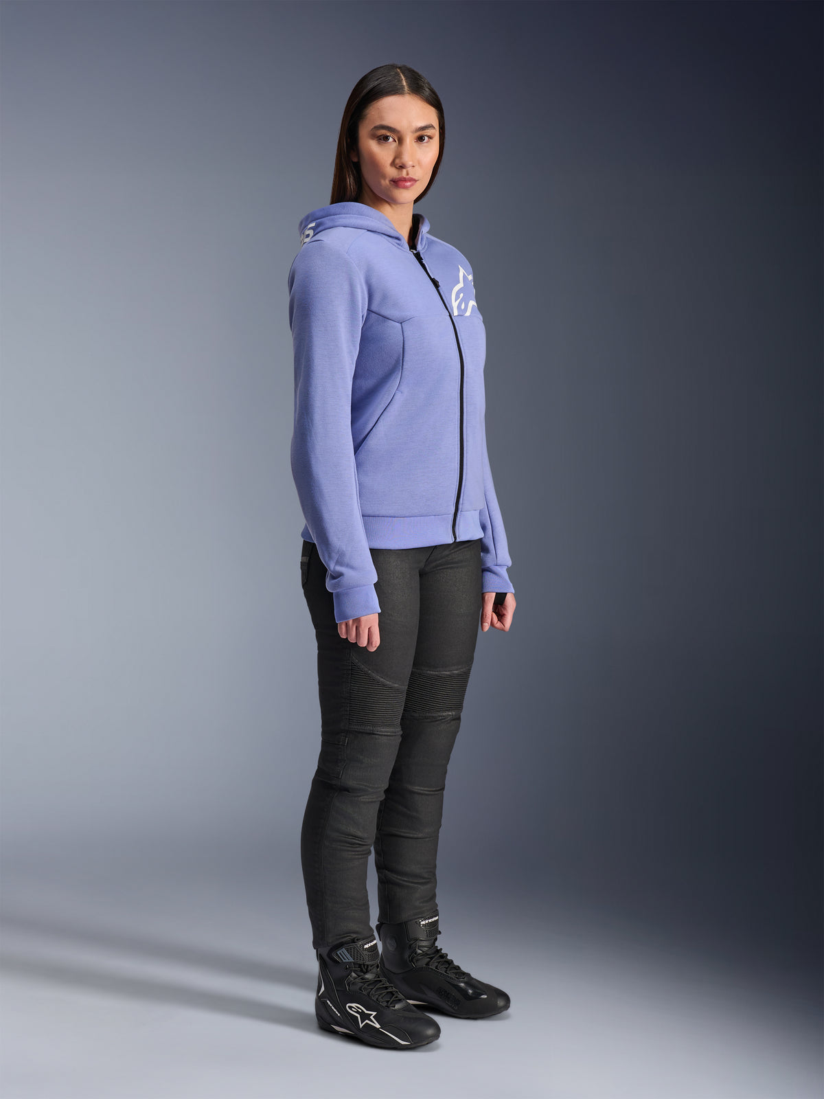 Alpinestars Stella Chrome V2 Sport Damen-Hoodie, Motorrad-Hoodie in Blau-Violett mit weißem Alpinestars-Logo auf der Brust, getragen von einem Modell mit schwarzer Motorradhose und schwarzen Motorradstiefeln, urbane Motorradbekleidung für Damen