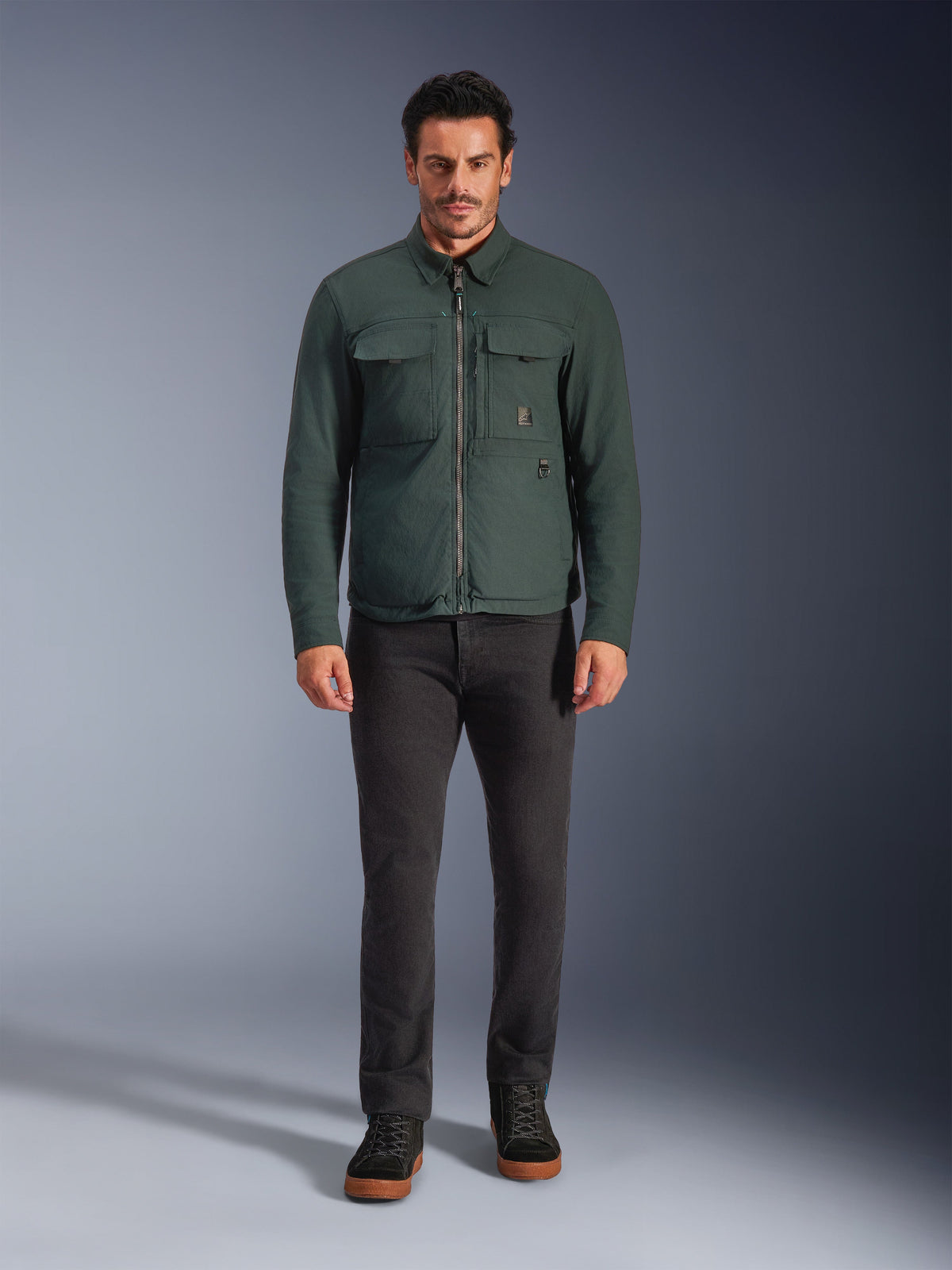 Alpinestars Bryon WR Overshirt, waterbestendig motorjack, Dark Emerald, gedragen met zwarte broek en zwarte laarzen, voorzien van een gewaxt canvas constructie, cargozakken op de borst en een modern urban design.