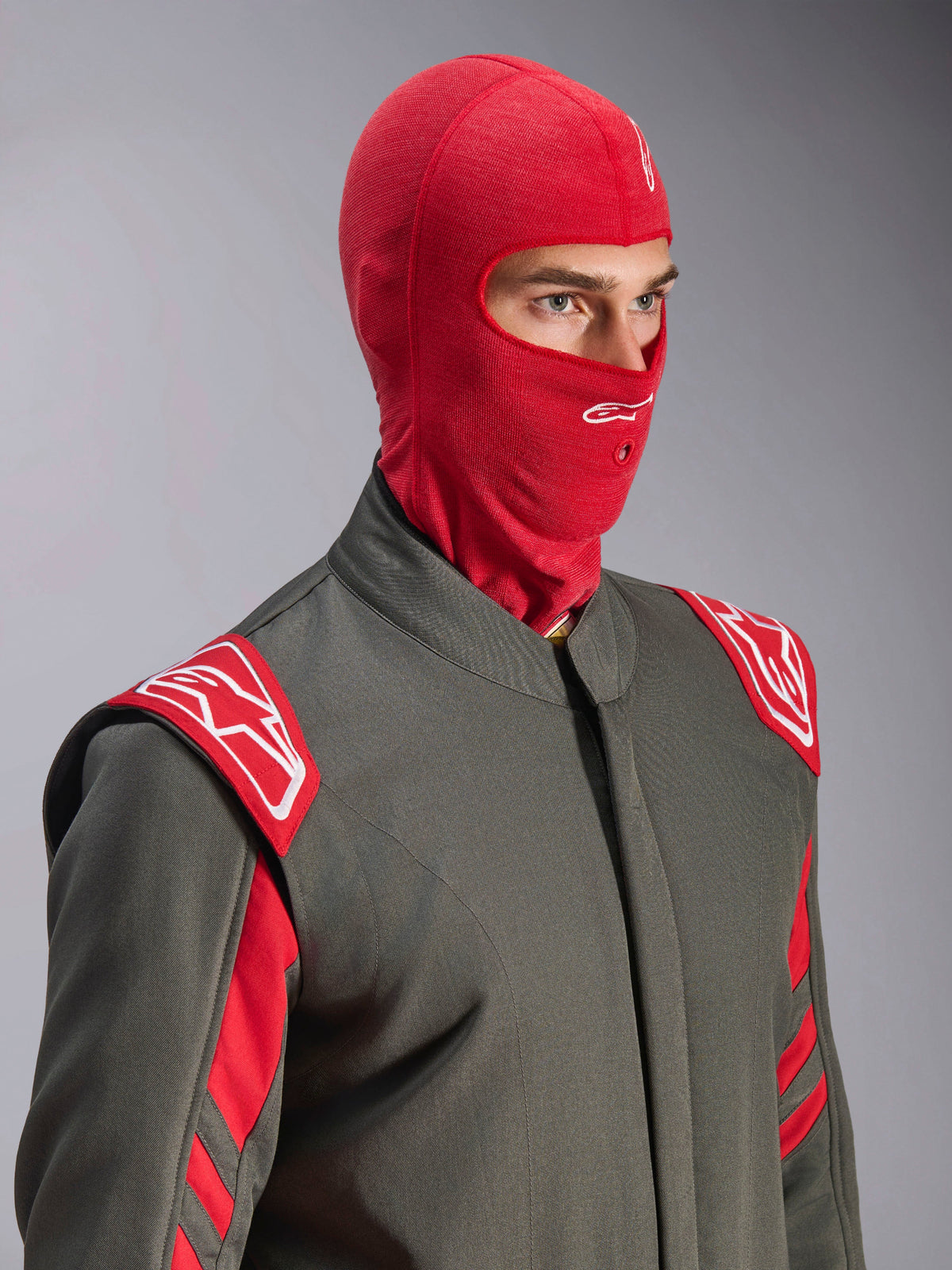 Cagoule Alpinestars ZX Evo V3, rouge, portée par un pilote dans une combinaison de course grise avec des accents rouges et blancs, arborant un logo Astars blanc sur le front et une ouverture pour tube d'hydratation, sous-couche résistante aux flammes pour la course automobile