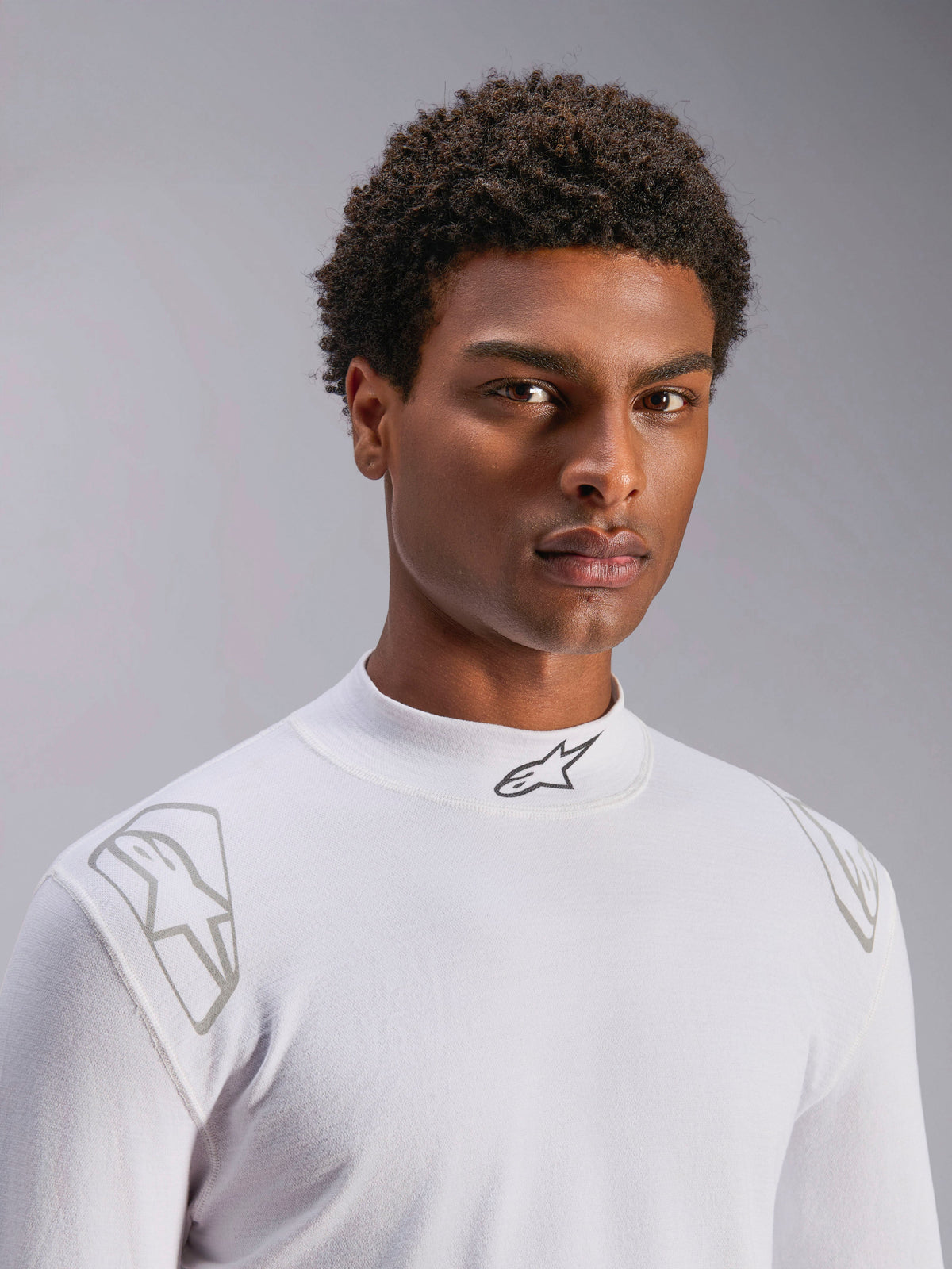 Haut à manches longues Alpinestars ZX Evo V3, sous-vêtement technique de course automobile blanc, porté par un mannequin homme, col montant avec logo Alpinestars noir, imprimés graphiques argentés sur les épaules, sous-vêtement de sport automobile léger et résistant aux flammes