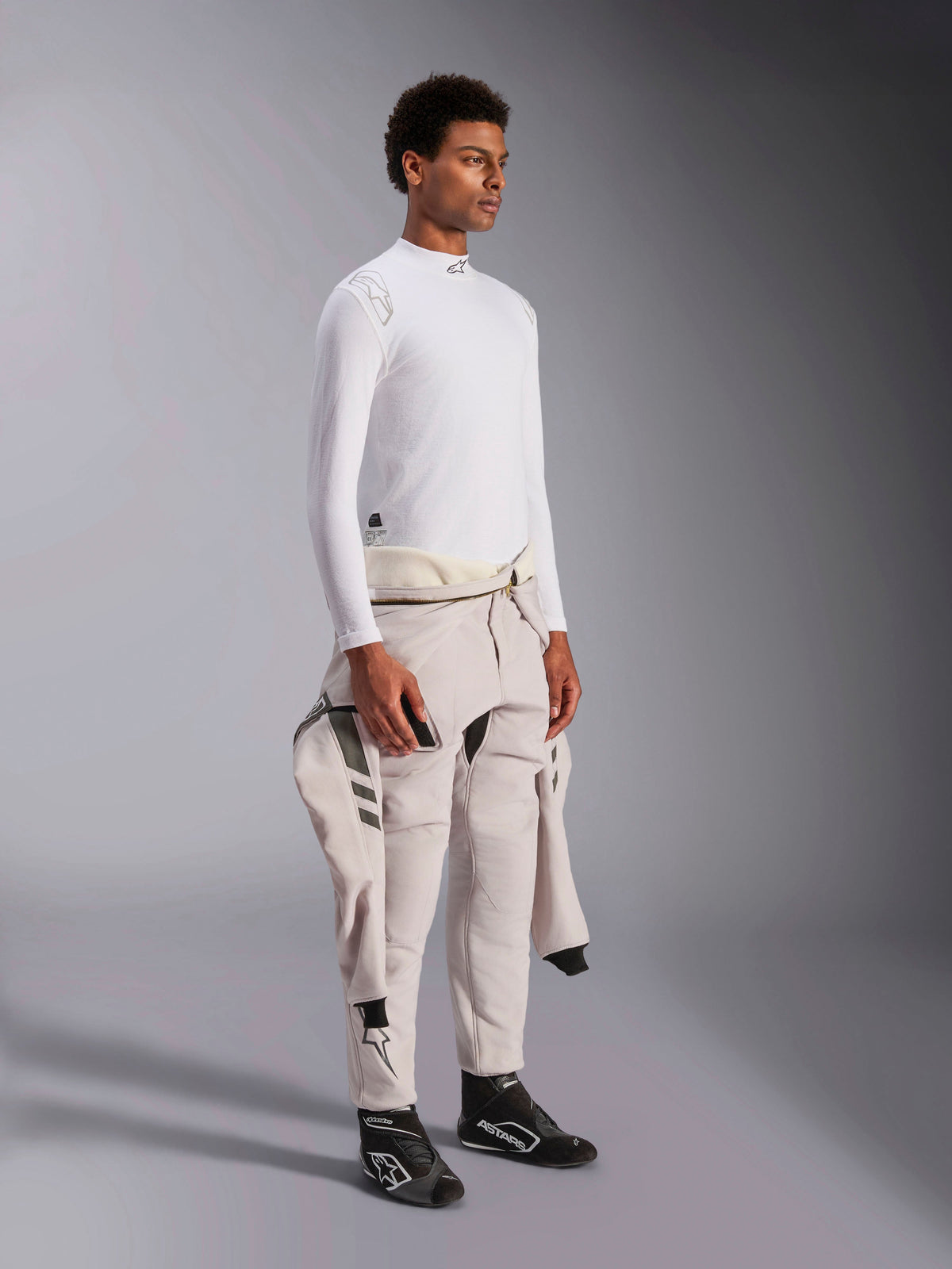 Haut à manches longues Alpinestars ZX Evo V3, sous-vêtement de course automobile blanc résistant aux flammes, porté par un mannequin avec une combinaison de course nouée autour de la taille, couche technique légère avec col montant et détails de logo.