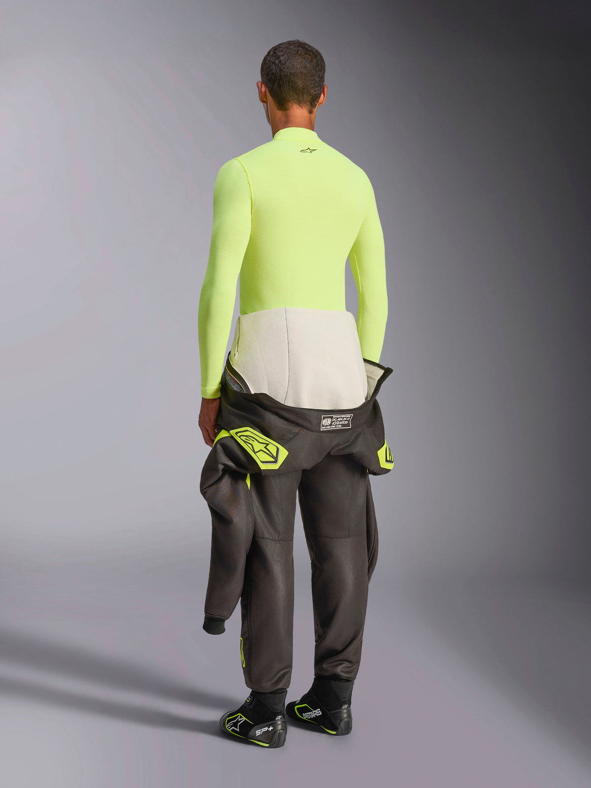 Alpinestars ZX Evo V3 Haut à manches longues, Jaune Fluo, vue arrière du mannequin portant une sous-couche résistante aux flammes avec pantalon de combinaison de course sombre et bottes, sous-vêtement technique professionnel pour le sport automobile