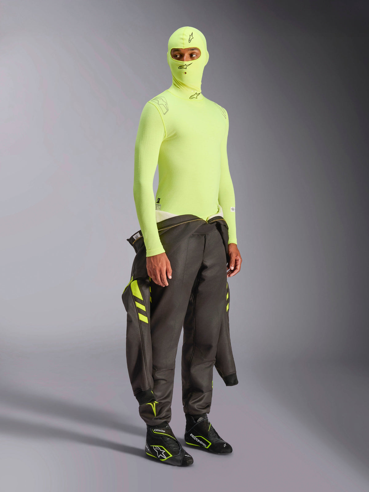 Haut à manches longues Alpinestars ZX Evo V3, jaune fluo, sous-vêtement technique pour le sport automobile porté avec une cagoule assortie et une combinaison de course sombre nouée à la taille, sous-vêtement ignifugé jaune fluo haute visibilité