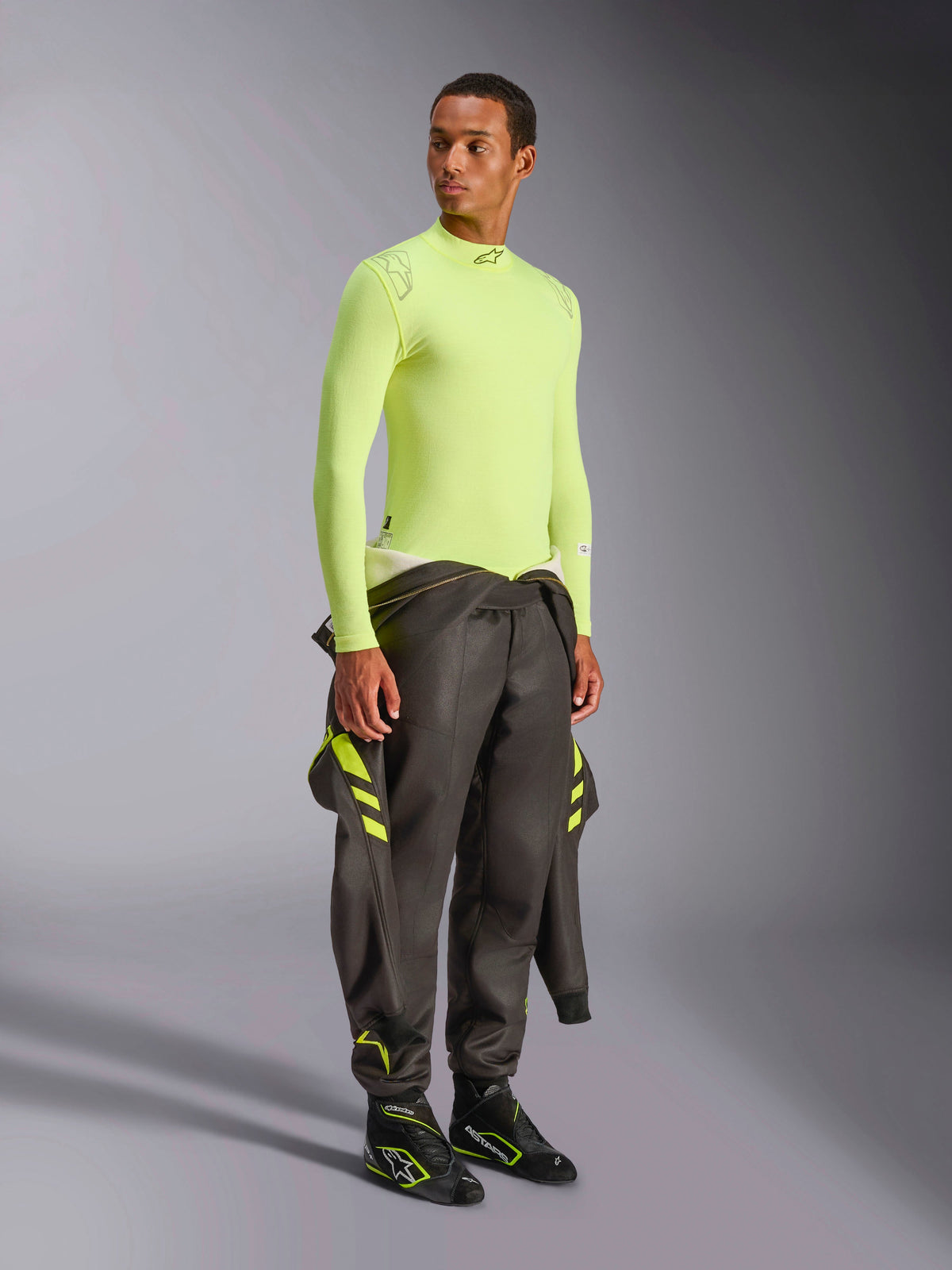 Alpinestars ZX Evo V3 Top - Manches Longues, Jaune Fluo, porté par un mannequin avec une combinaison de course gris foncé nouée à la taille et des bottes de course noires, sous-couche de sport automobile résistante aux flammes, construction légère en maille jacquard, équipement de course automobile professionnel