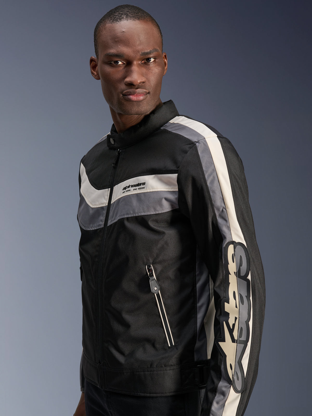 Alpinestars T-Dyno WR Jas, zwart, donkergrijs en ecru, vintage-geïnspireerde textiele motorjas met horizontale strepen op de borst, groot verticaal logo op de mouw en voorzakken met ritssluiting, urban motorkleding