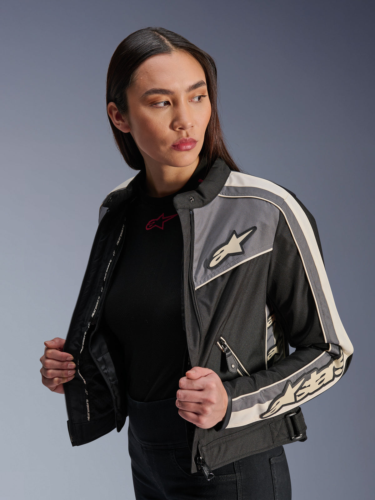 Veste Alpinestars Stella T-Dyno WR pour femme, veste de moto en textile, noir, gris foncé et écru, design d'inspiration vintage avec des bandes sportives et des logos sur la poitrine et les manches, portée par un mannequin, équipement de route urbain