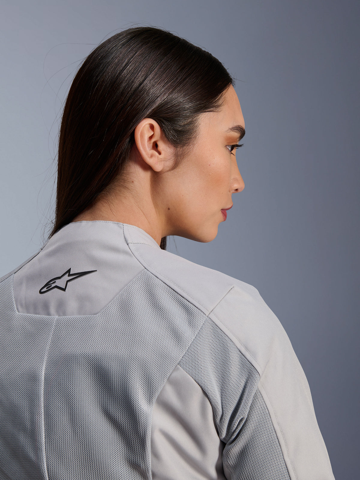 Woman wearing the Alpinestars Stella C-1 Air Jacket in Silver, close-up side-back view showing the black Alpinestars logo, tech mesh ventilation panels, and a clean contemporary urban motorcycle design.