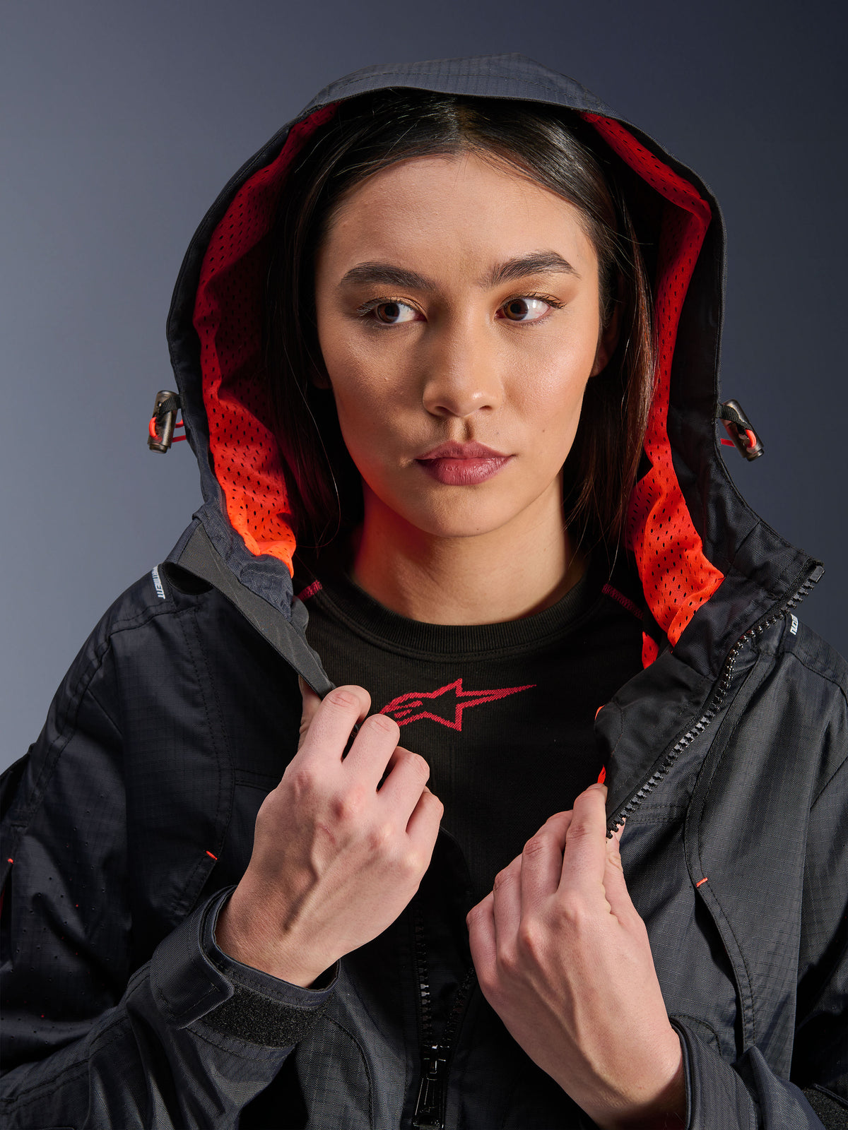 Alpinestars Molly Air Jacke, Damen-Motorradjacke, Schwarz und Fluo Coral, Modell trägt die Kapuze oben und zeigt das leuchtende korallenfarbene Mesh-Innenfutter, Ripstop-Textilgewebe, urbane zeitgemäße Motorradbekleidung