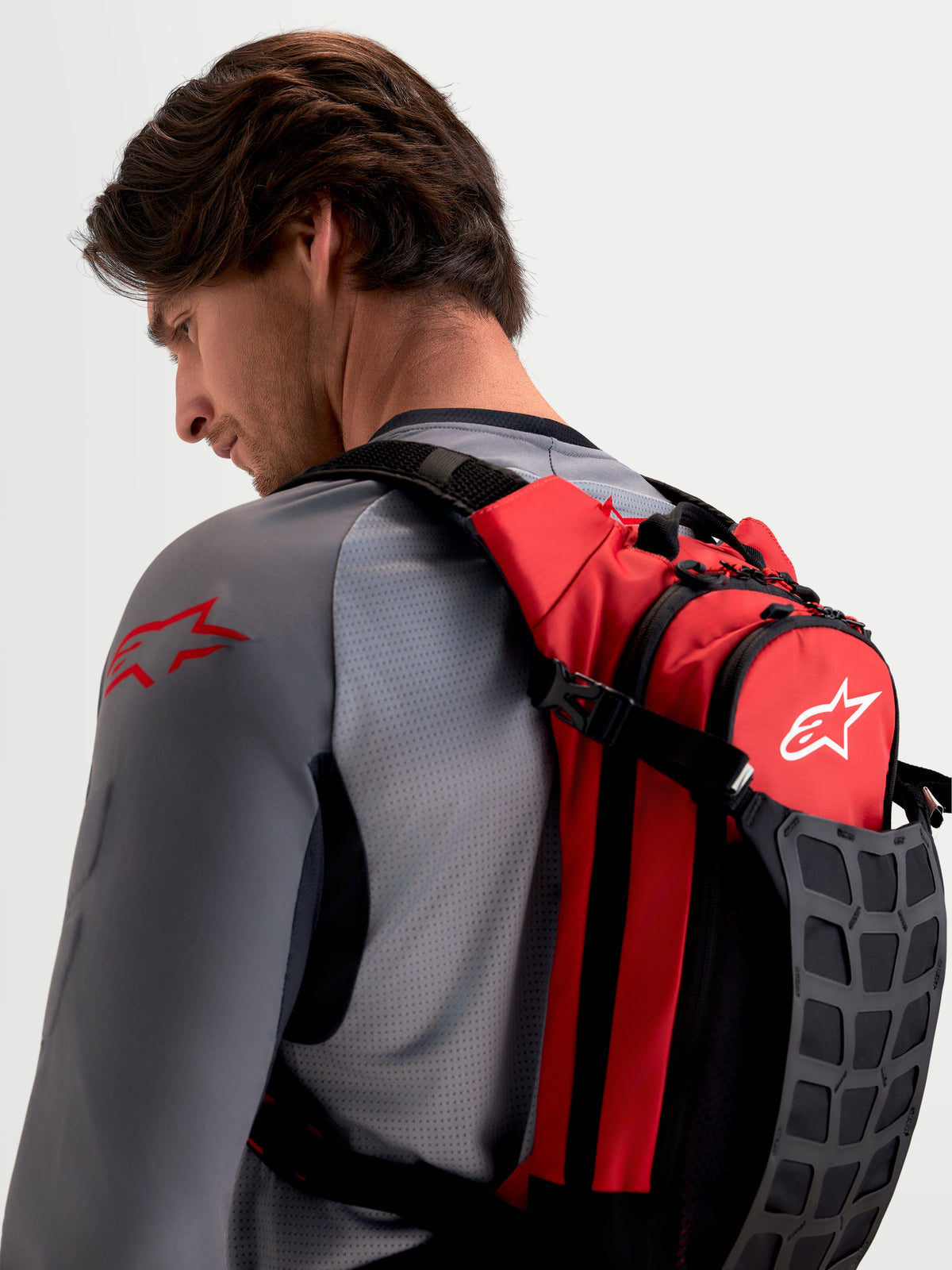 Alpinestars AT-9 Rucksack, Motocross-Rucksack in Rot und Schwarz, getragen von einem männlichen Model, mit gepolsterten Schultergurten und organisierter Aufbewahrung für Strecken-Essentials