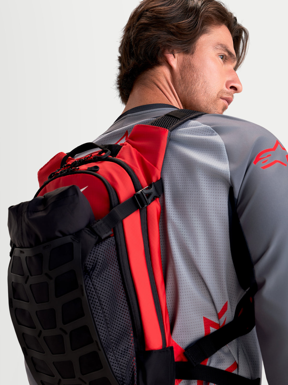 Alpinestars AT-9 Rucksack, Motocross-Rucksack in Schwarz und Leuchtrot, Rückansicht an einem Model, das die leichte Textilkonstruktion und die gepolsterten Schultergurte präsentiert