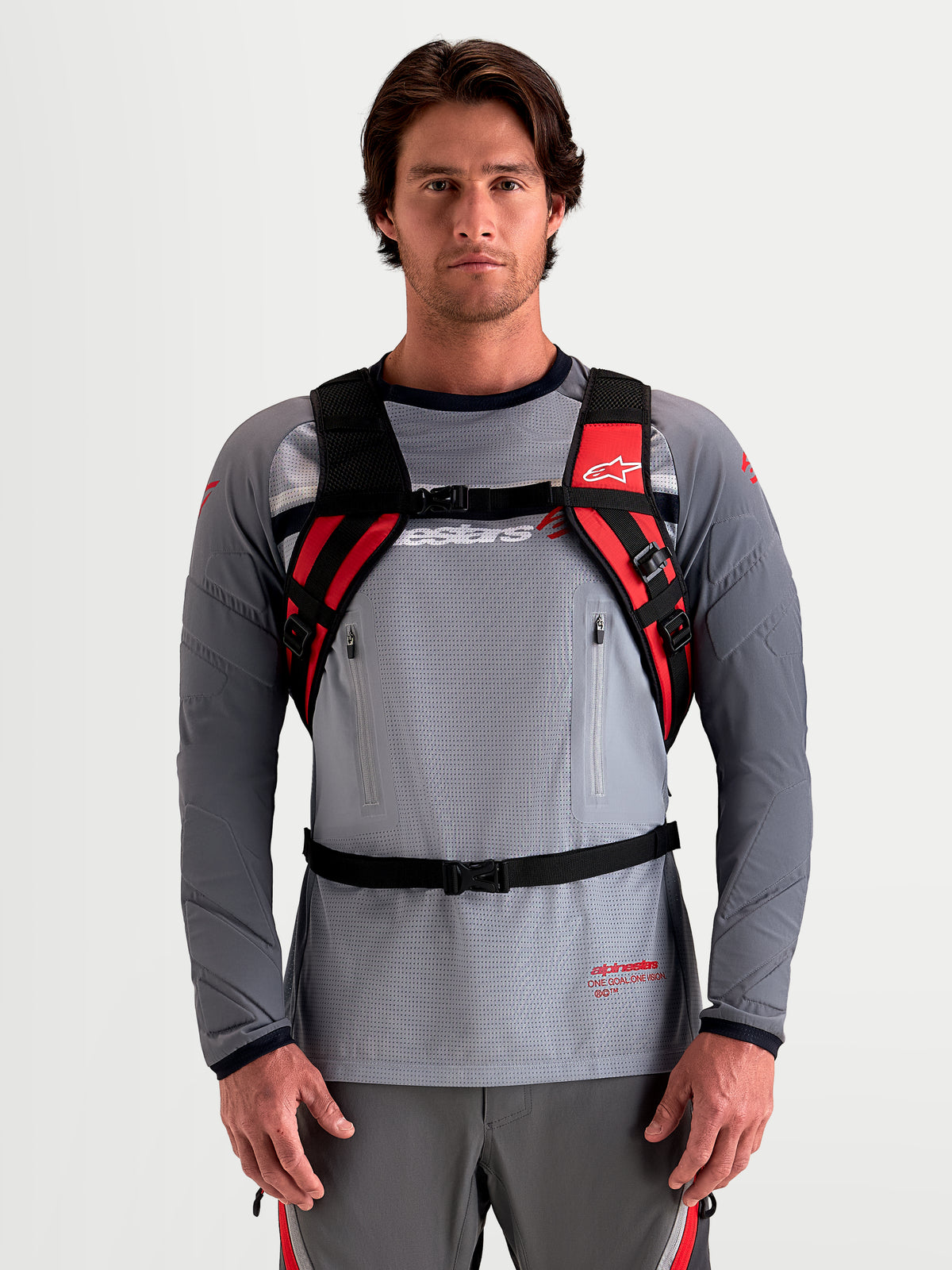 Alpinestars AT-9 Rucksack, Motocross-Rucksack in Schwarz und Leuchtrot, getragen von einem männlichen Model mit gepolsterten Schultergurten und Gurtsystem, leichte Textilkonstruktion